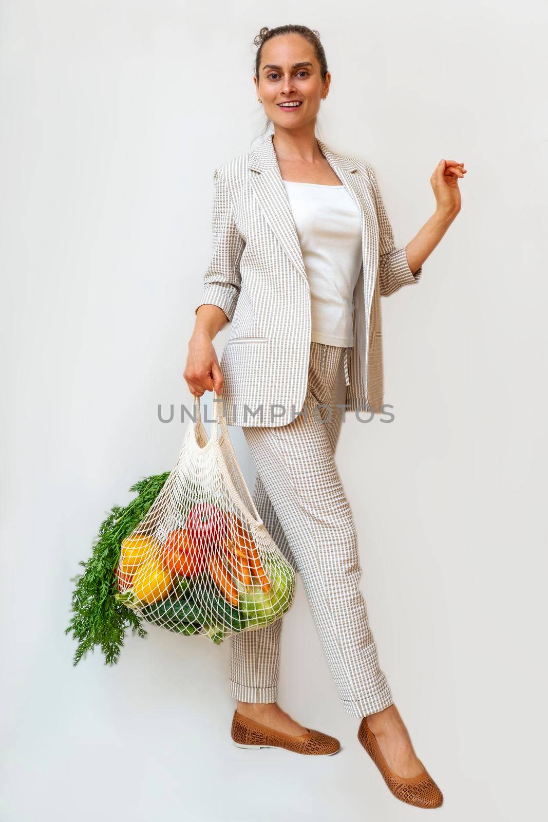 A woman in a light suit holds a cotton shopper and reusable mesh shopping bags with vegetables. Zero waste without plastic concept with copy space. Eco-friendly net buyer.
