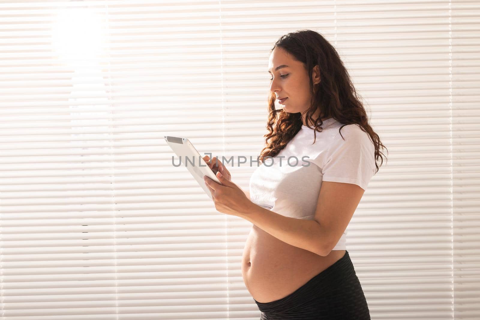 Happy pregnant young beautiful woman talking to her husband using video connection and tablet. Communication and positive attitude during pregnancy