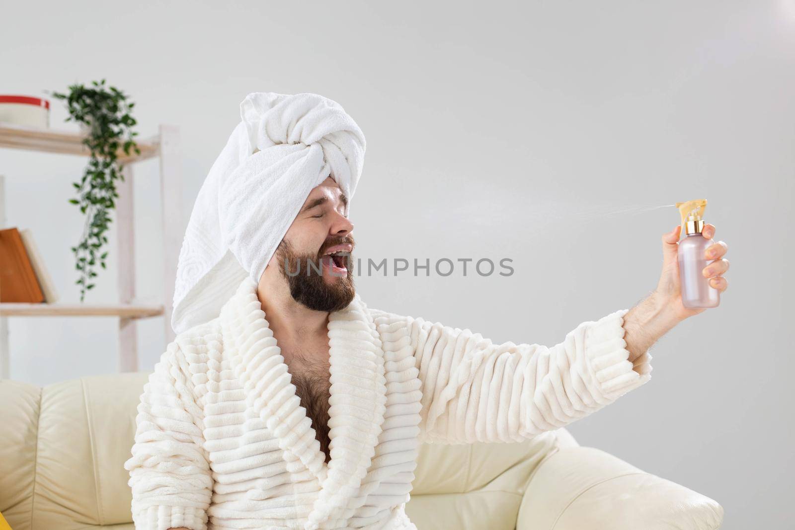 Bearded male with bath towel on his head applying spray water treatment on face. Spa, body and skin care for man concept