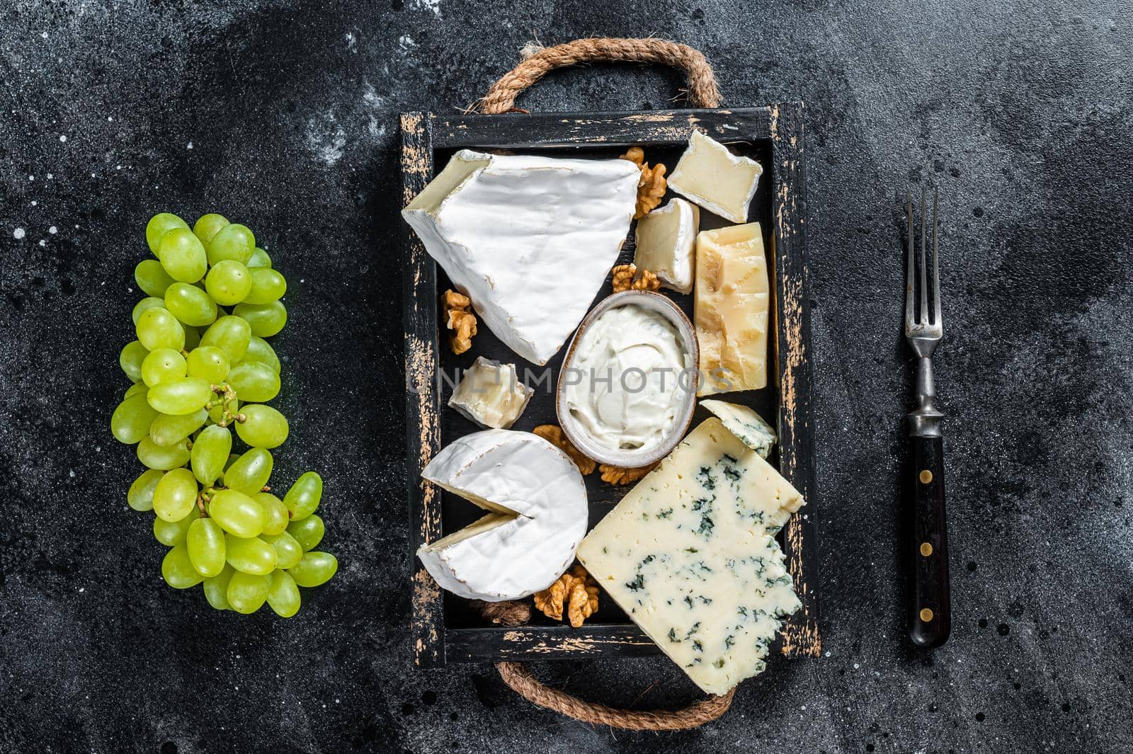 Assorted Cheese platter with Brie, Camembert, Roquefort, parmesan, blue cream cheese, grape and nuts. Black background. Top view.