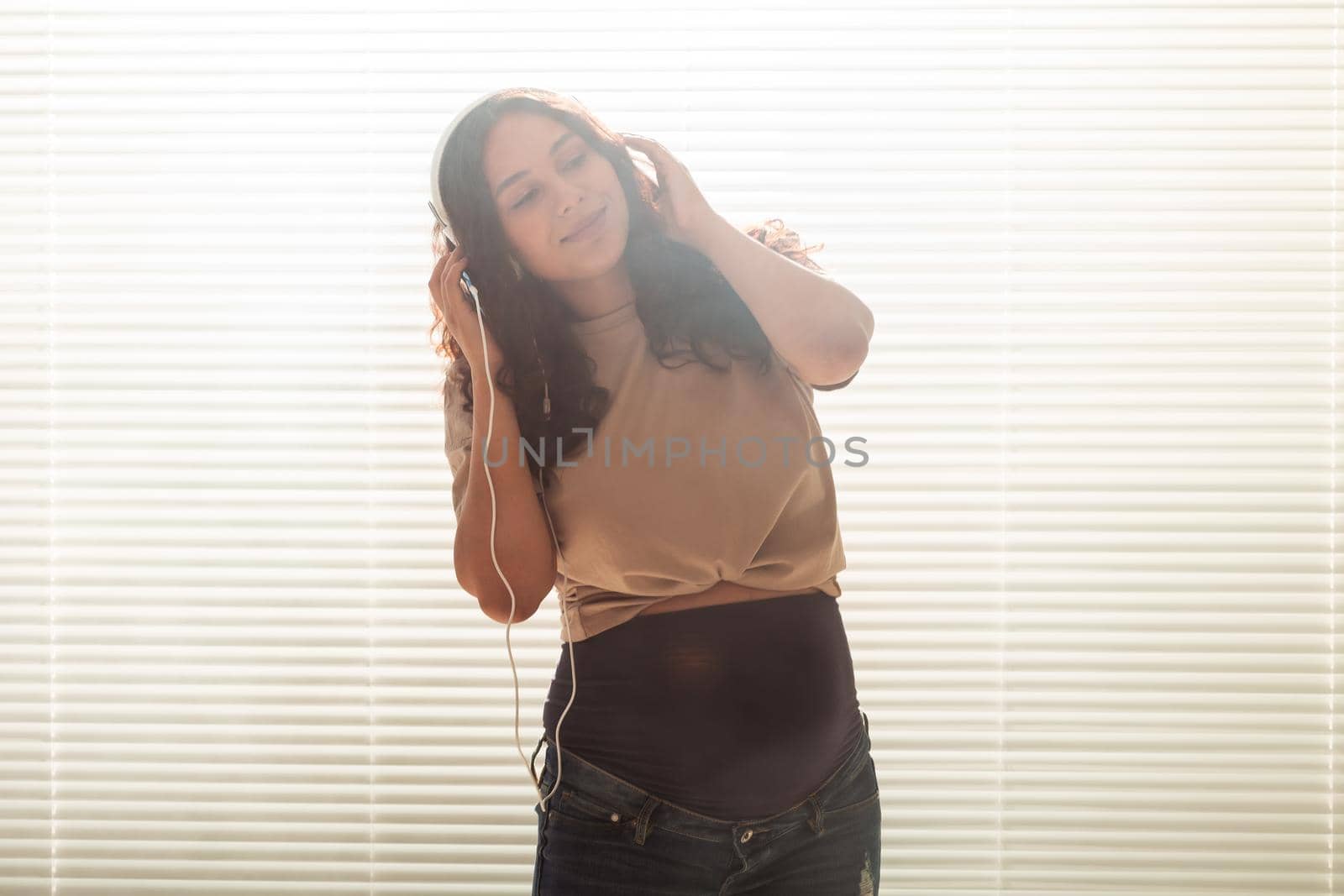 Portrait of pregnant woman sitting on sofa at home and listening music in headphones.