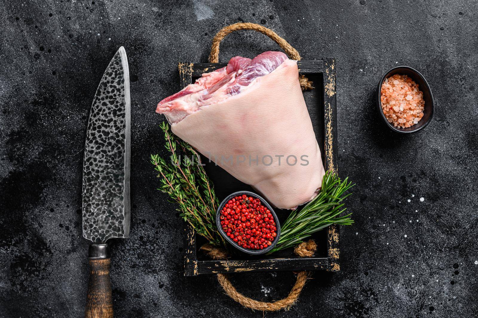 Fresh Raw pork Eisbein knuckle ham in a wooden tray with meat knife. Black Wooden background. Top view.