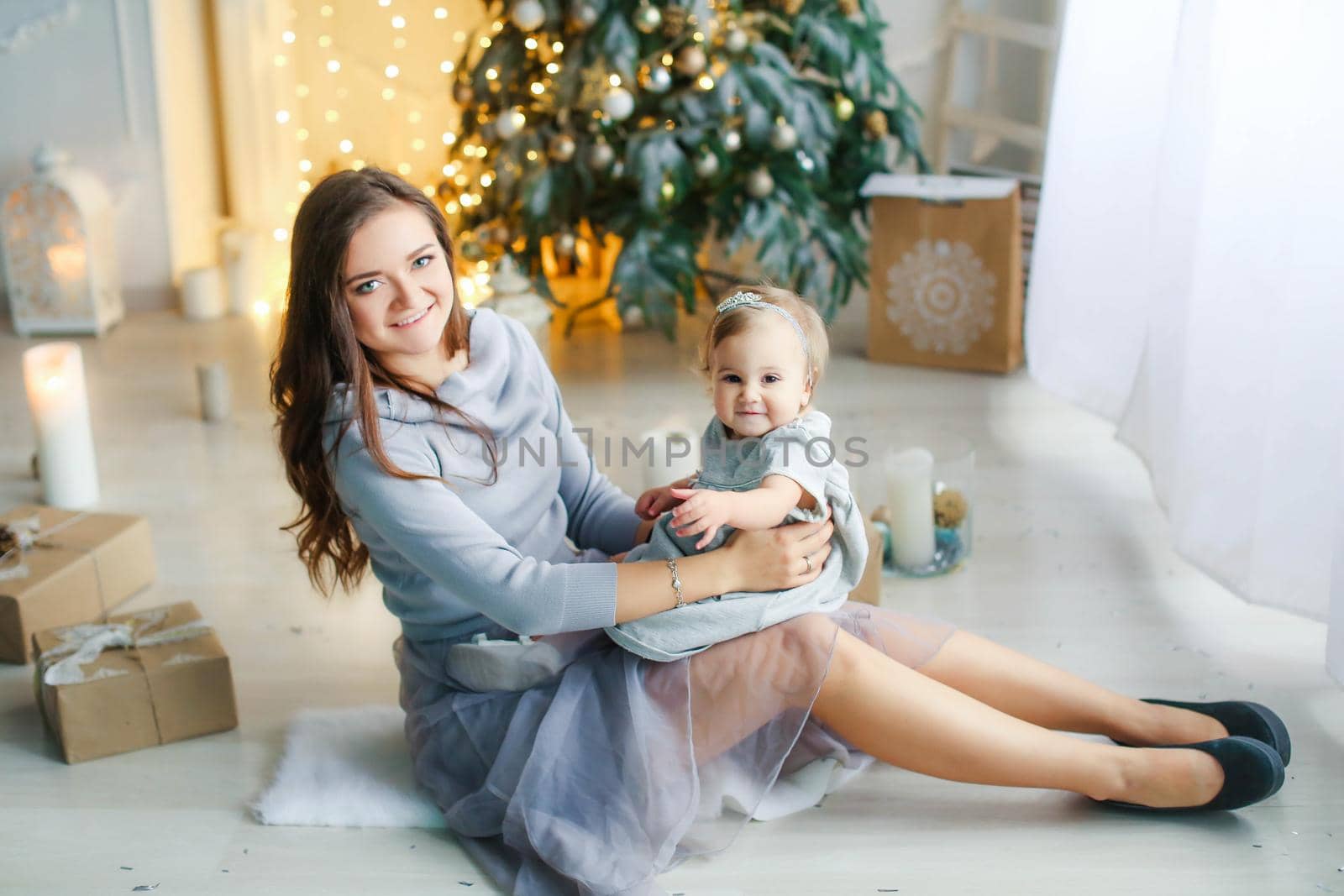 Family of two people mother and daughter 1 year old against the background of the Christmas tree photo in bright colors.