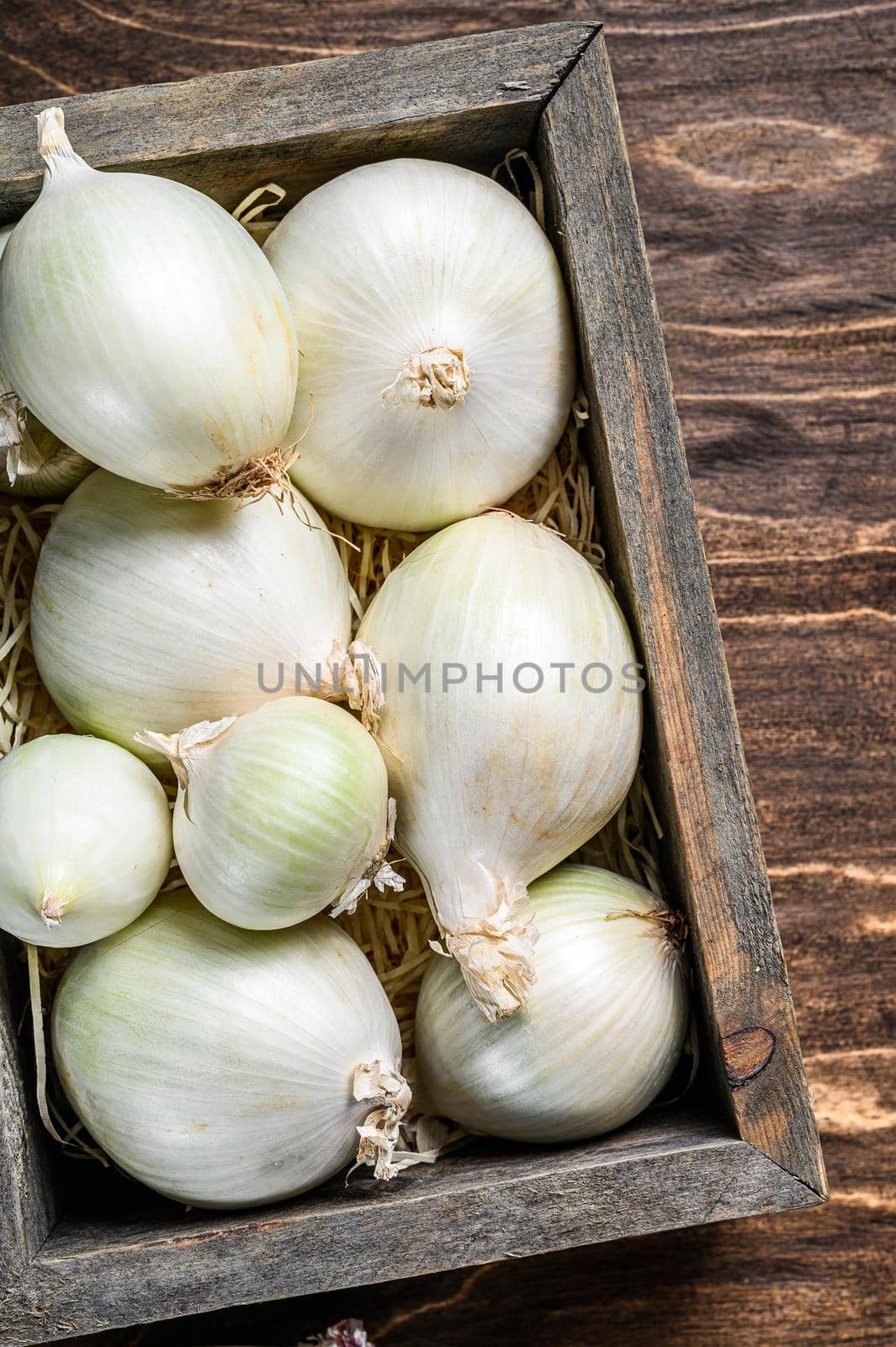 Raw fresh white onion in wooden box. Wooden background. Top view by Composter