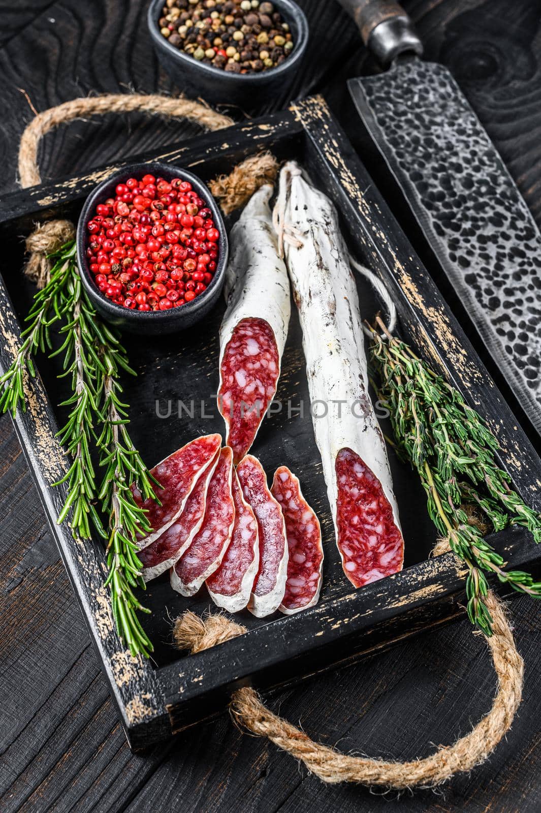 Fuet Salami sausage slices with thyme and rosemary in a wooden tray. Black wooden background. Top view by Composter