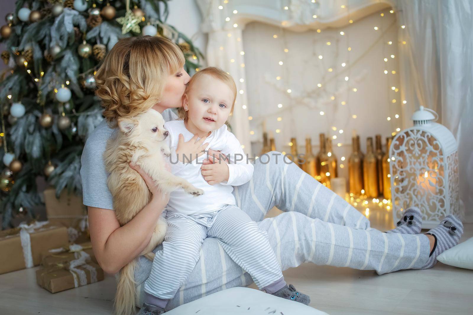 Child and mother in light pajamas on the background of a Christmas tree.