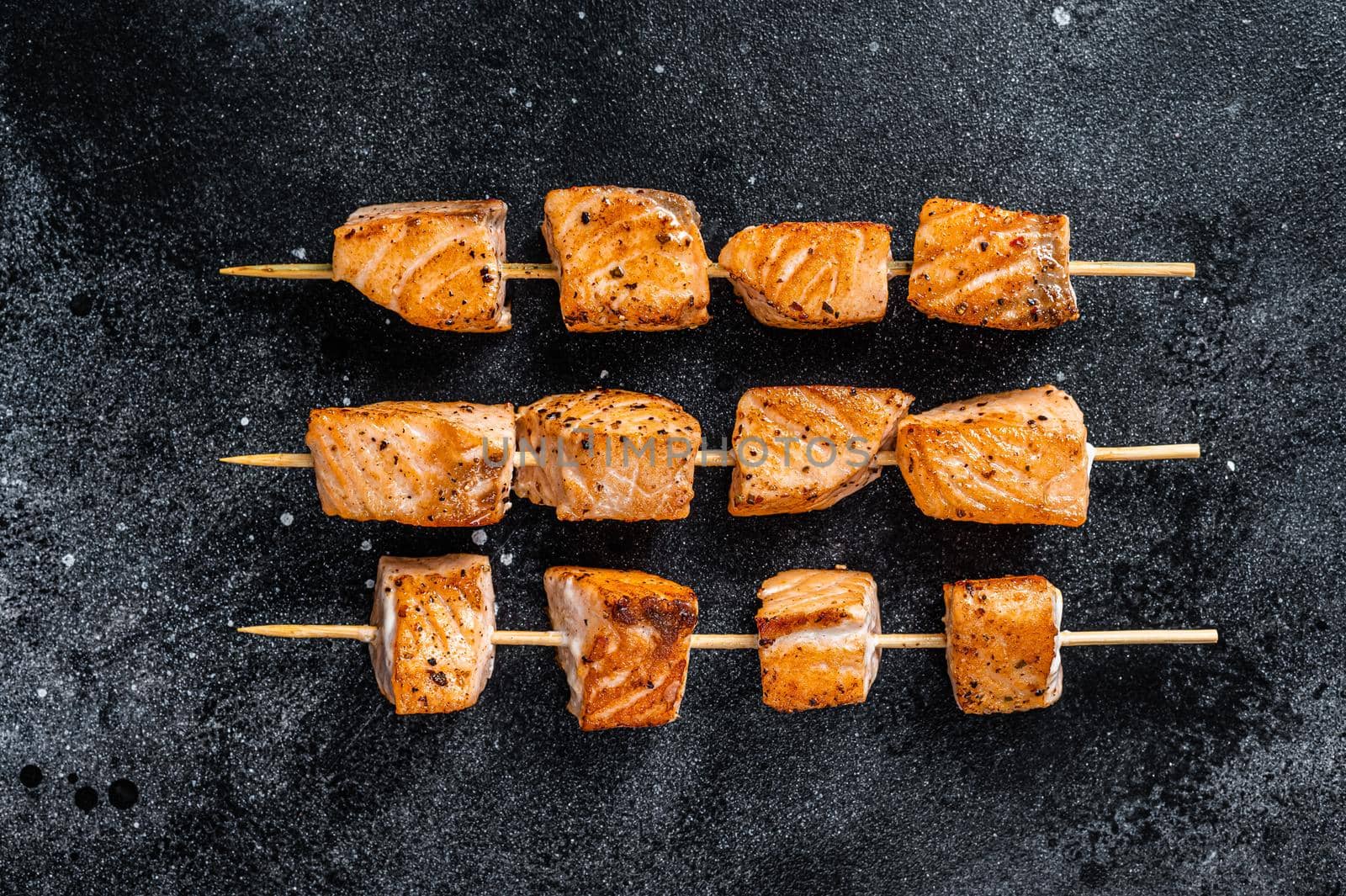 Grilled salmon kebab skewers. Black background. Top View.