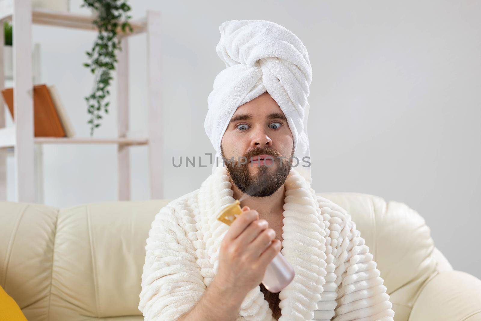 Bearded male with bath towel on his head applying spray water treatment on face. Spa, body and skin care for man concept