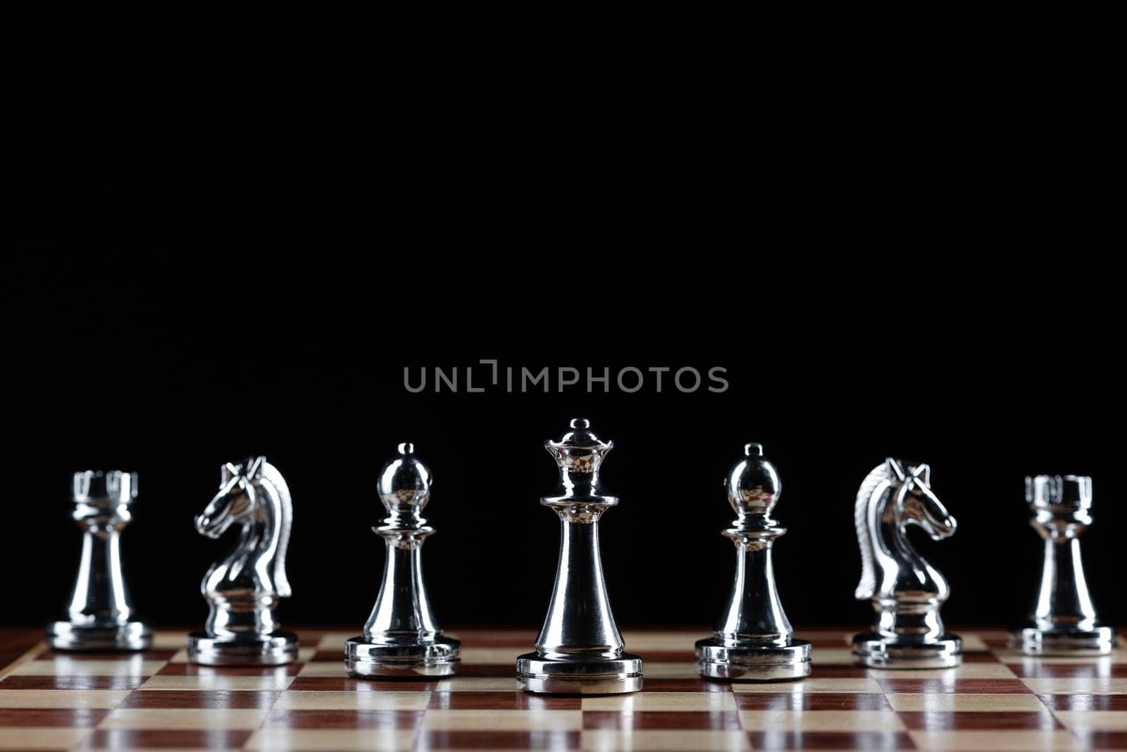 Silvery chess figures standing on chessboard. Intellectual competition and fight in business. Strategy planning and leadership concept with copy space. Silver chess pieces in row on black background.