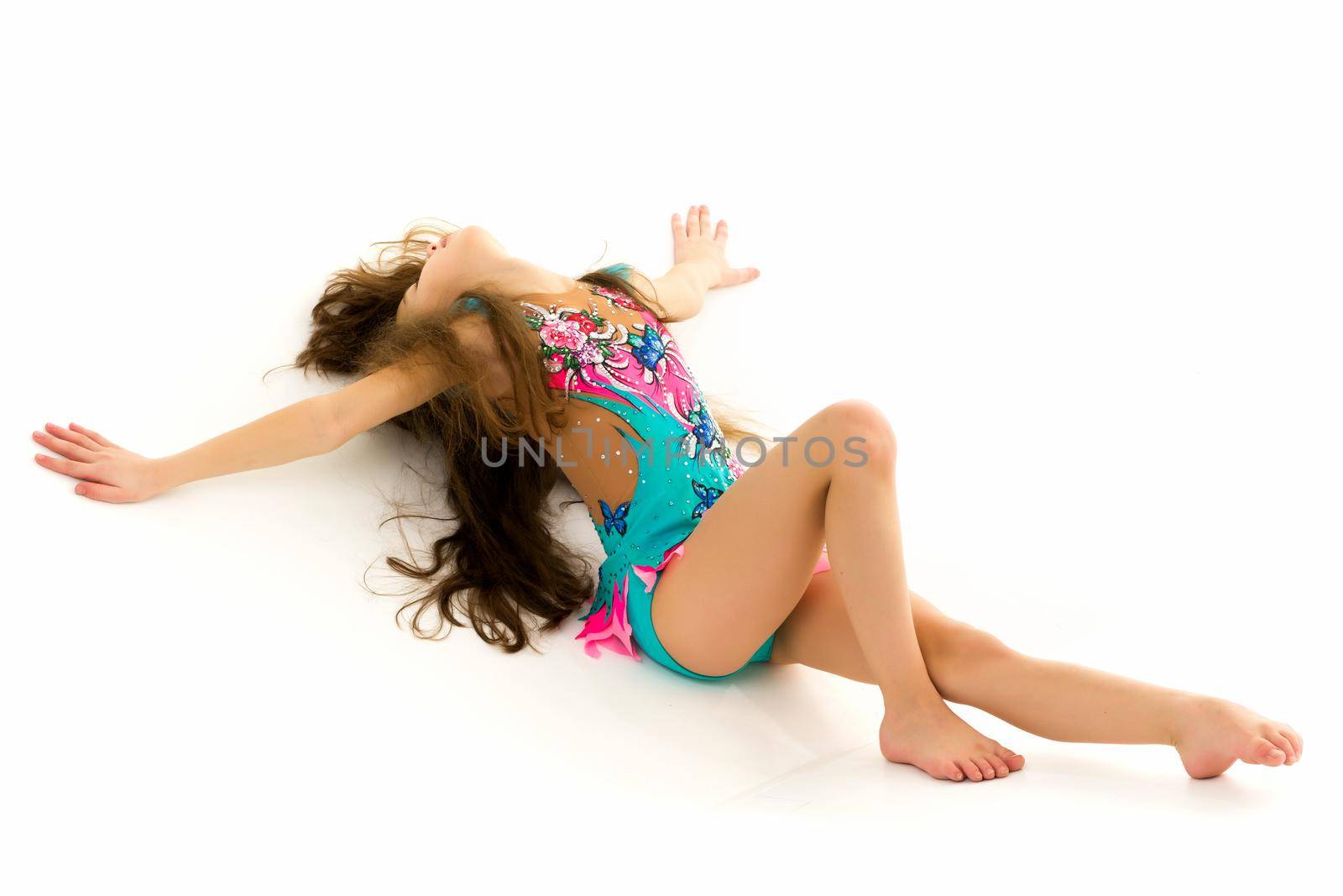 Cute little girl performs gymnastic exercises on the floor in the studio on a white background. The concept of sports, the physical development of children