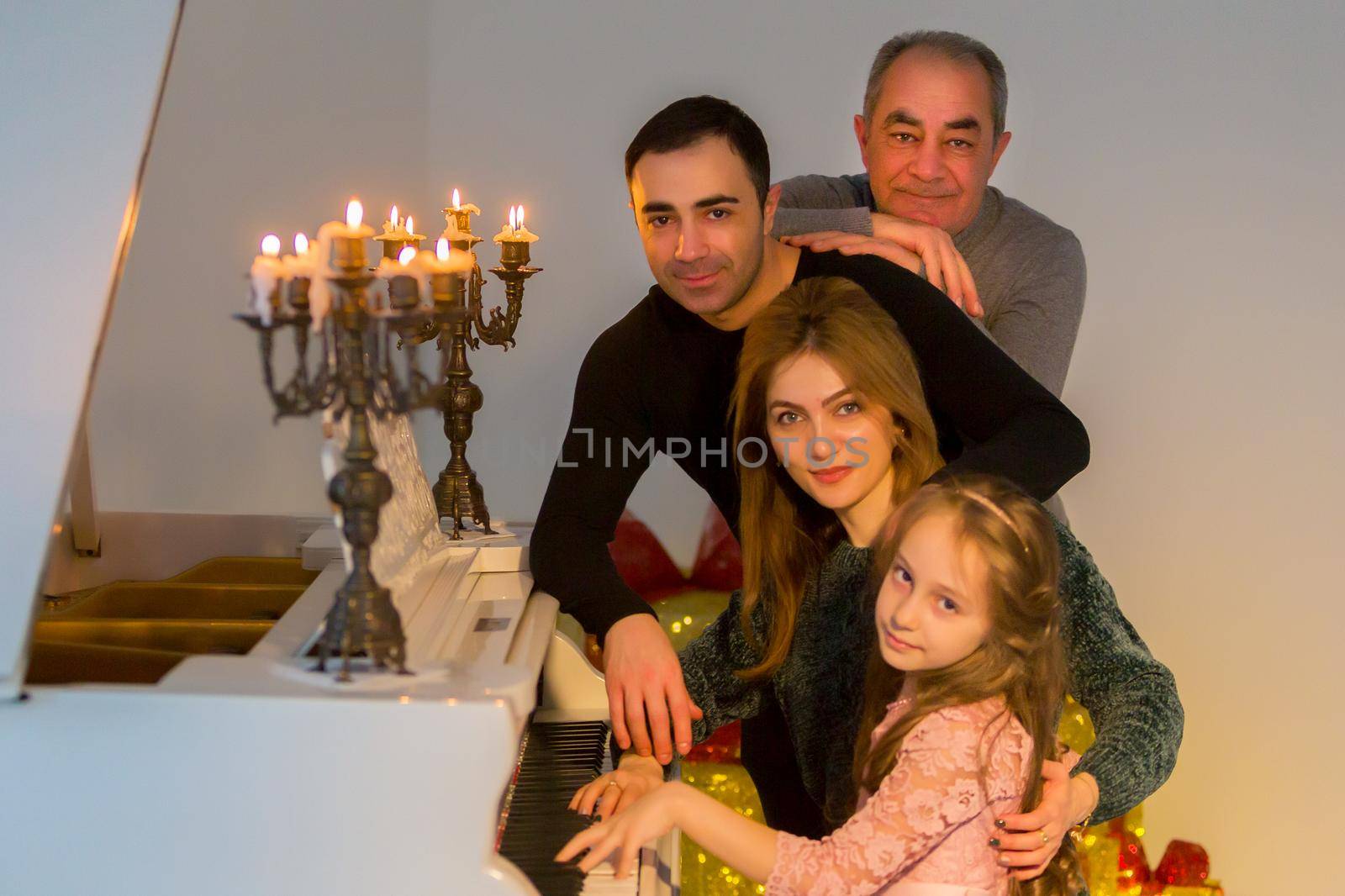 Portrait of Three Generation Family, Parents, Their Adorable Daughter and Grandfather Posing near Grand Piano Decorated with Burning Candles in Candlesticks, Family Members Hugging, Looking at Camera