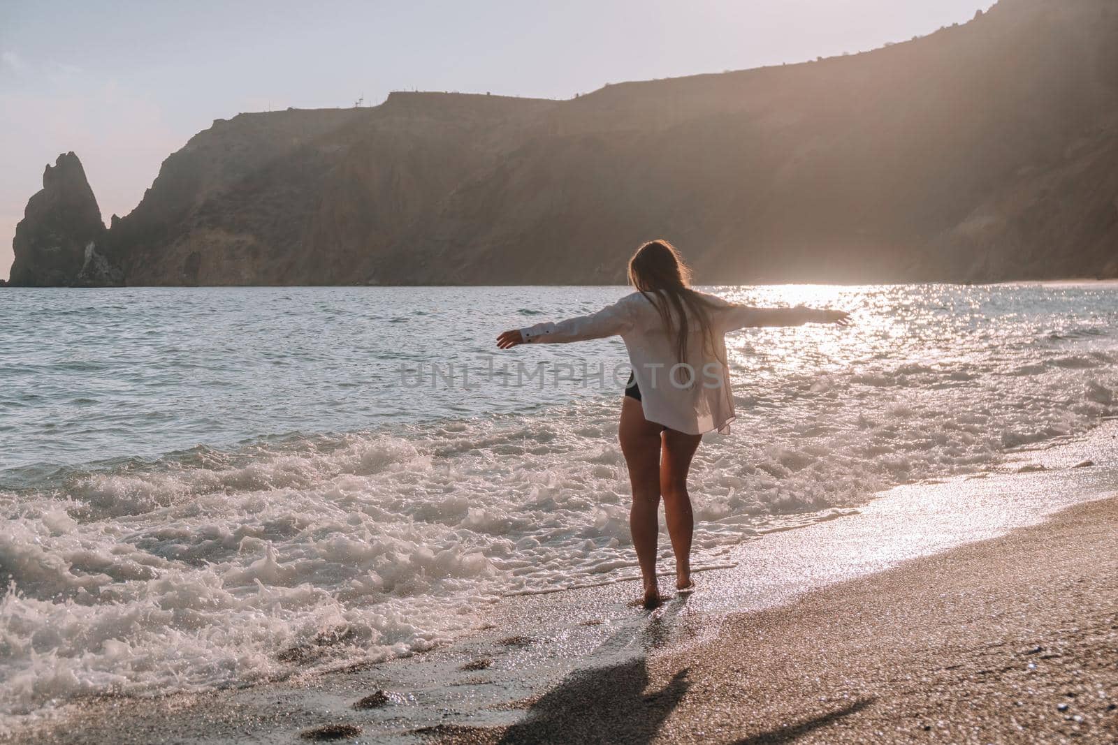 Selective focus. Happy carefree sensual woman with long hair in black swimwear posing at sunset beach. Silhouette of young beautiful playful positive woman outdoor. Summer vacation and trip concept.