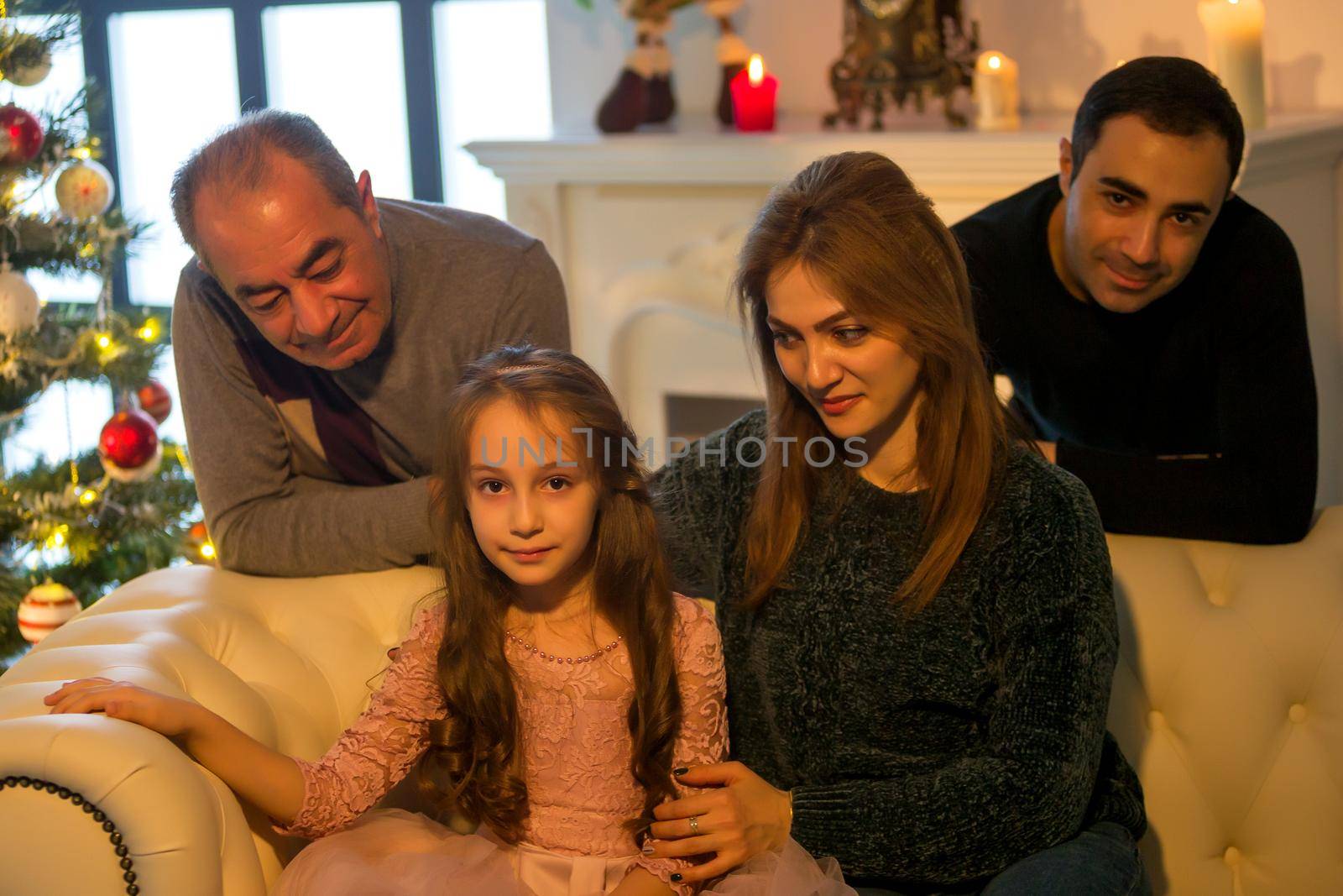 Parents hug their adorable daughter, mom and dad, as well as grandfather near the tree. by kolesnikov_studio