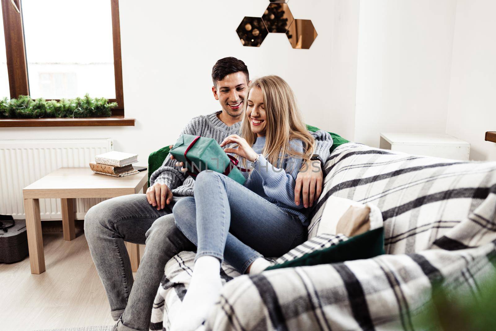 Sweet young couple opening Christmas gifts in the living room at home