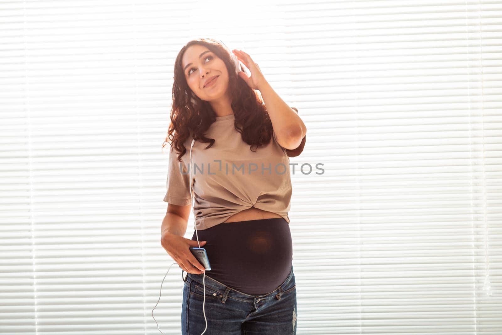 Young peaceful pregnant woman listens to pleasant classical music using smartphone and headphones. Concept of positive attitude before childbirth