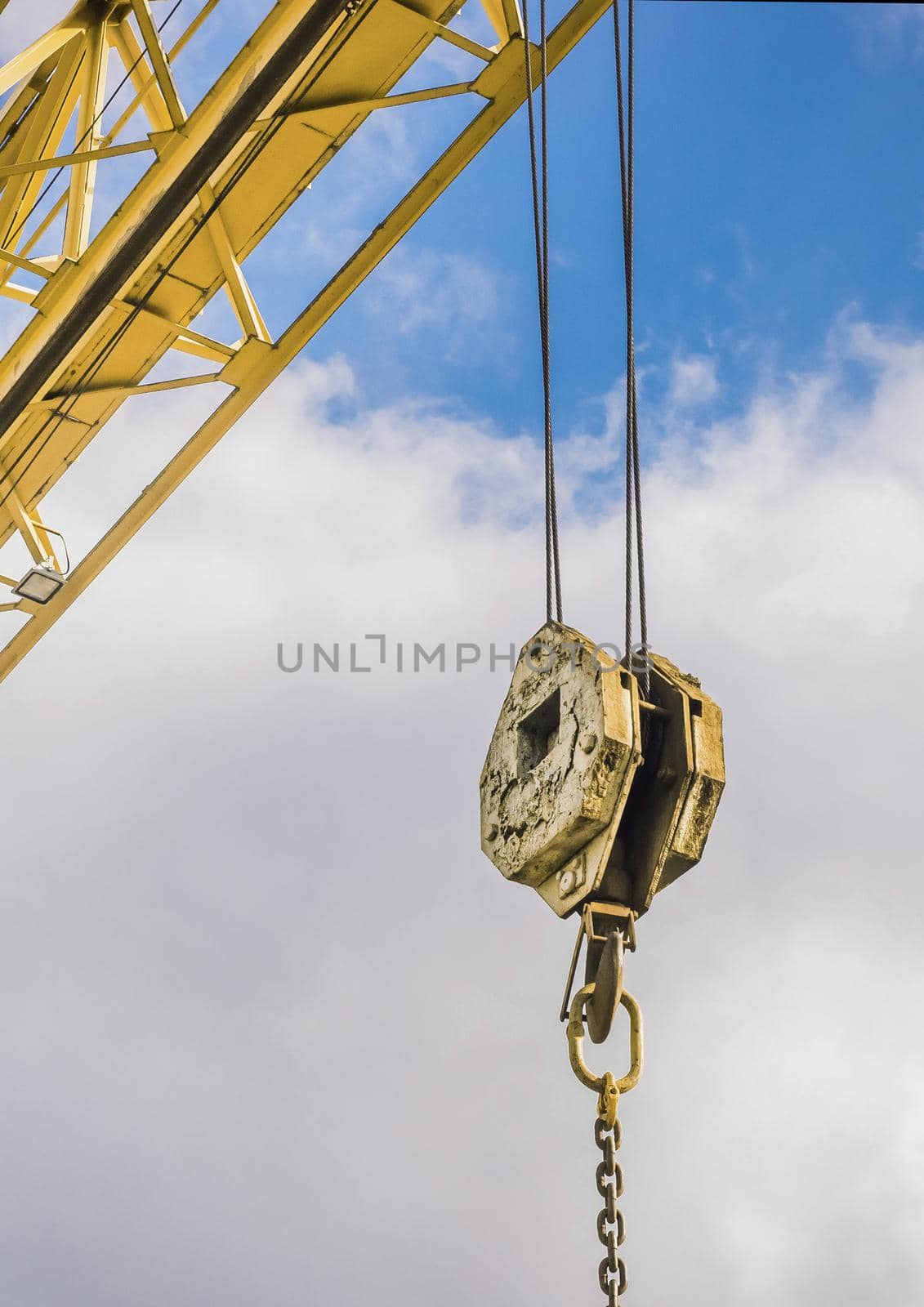 Overhead crane hoist industrial mechanism with hook and chain on a background of blue sky with clouds, close-up.