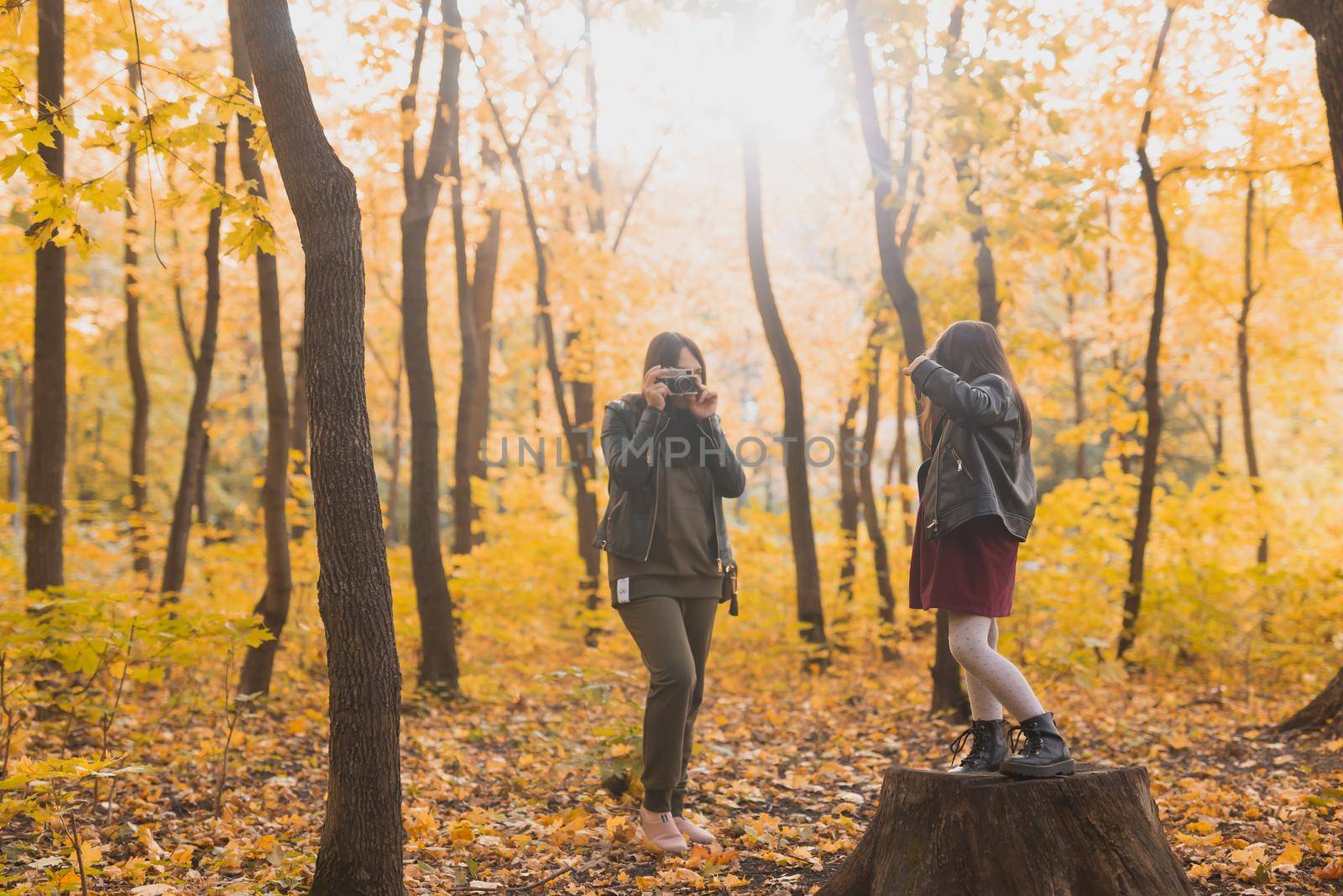 Mother photographer takes pictures of a her daughter in the park in autumn. Hobbies, photo art and leisure concept. by Satura86