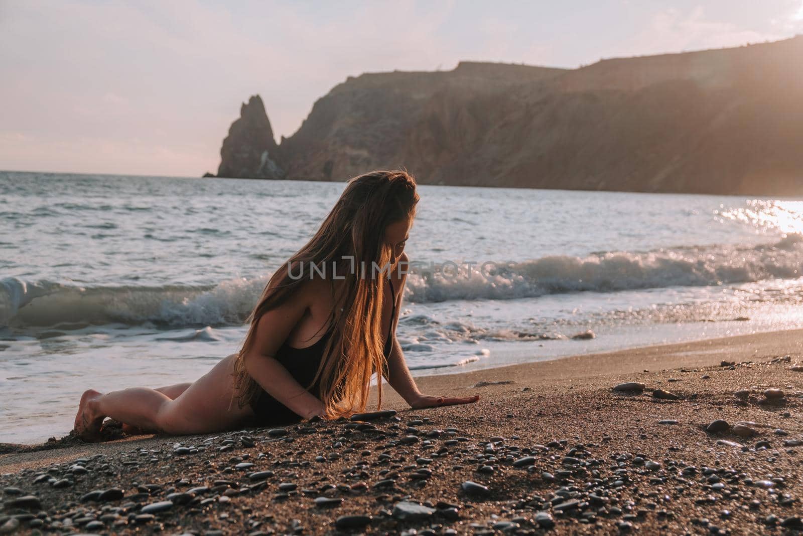 Selective focus. Happy carefree sensual woman with long hair in black swimwear posing at sunset beach. Silhouette of young beautiful playful positive woman outdoor. Summer vacation and trip concept.