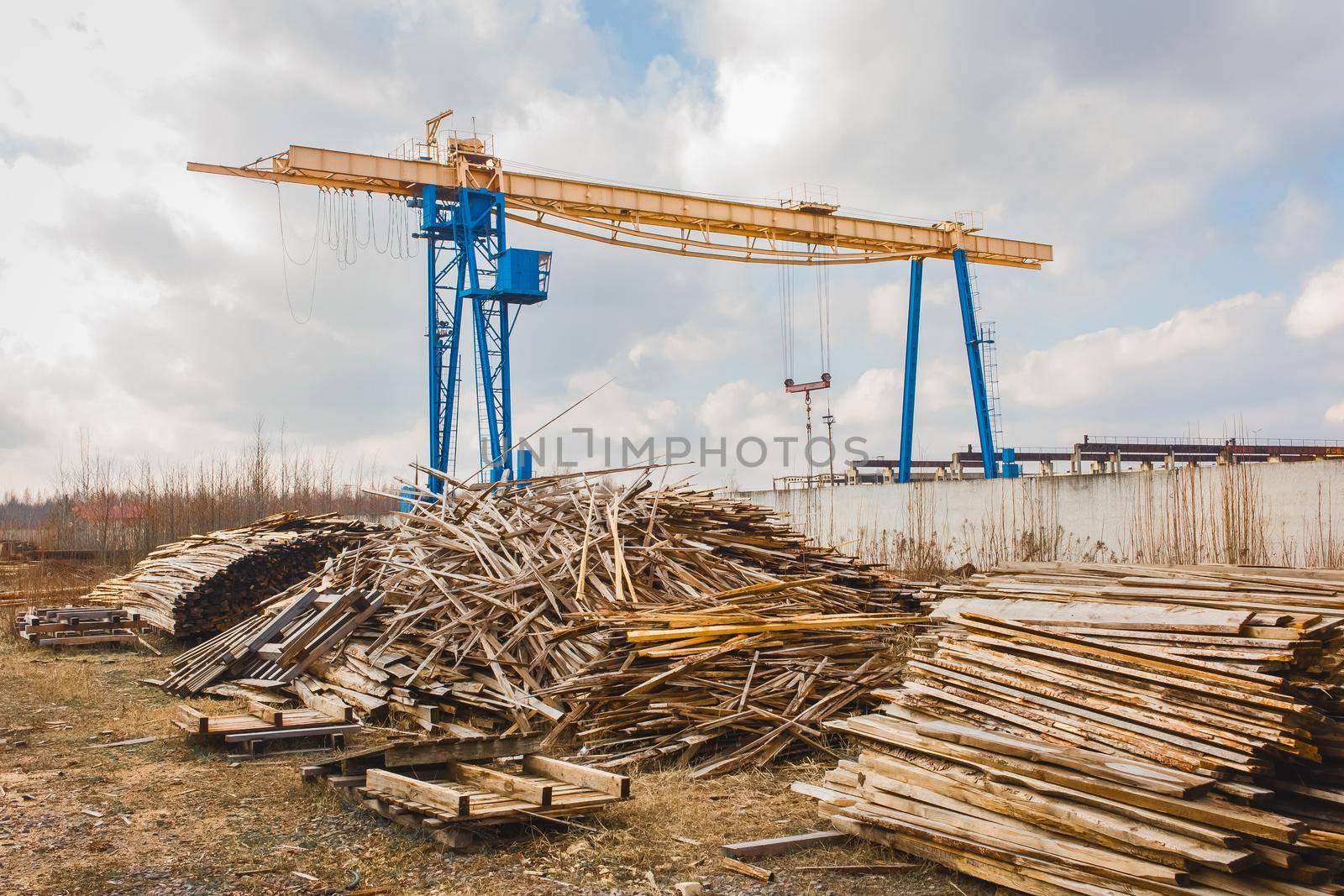 Industrial zone, construction site with piles of wooden waste and overhead hoist building crane.