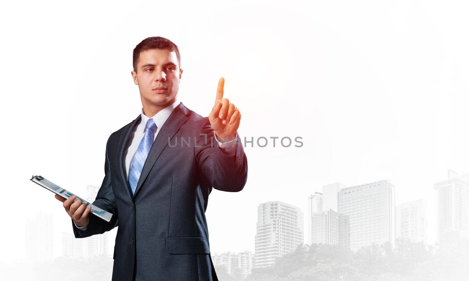 Handsome businessman standing and finger pointing at something. Front view of man in business suit and tie on background foggy cityscape. Successful business person in formal wear with raised hand