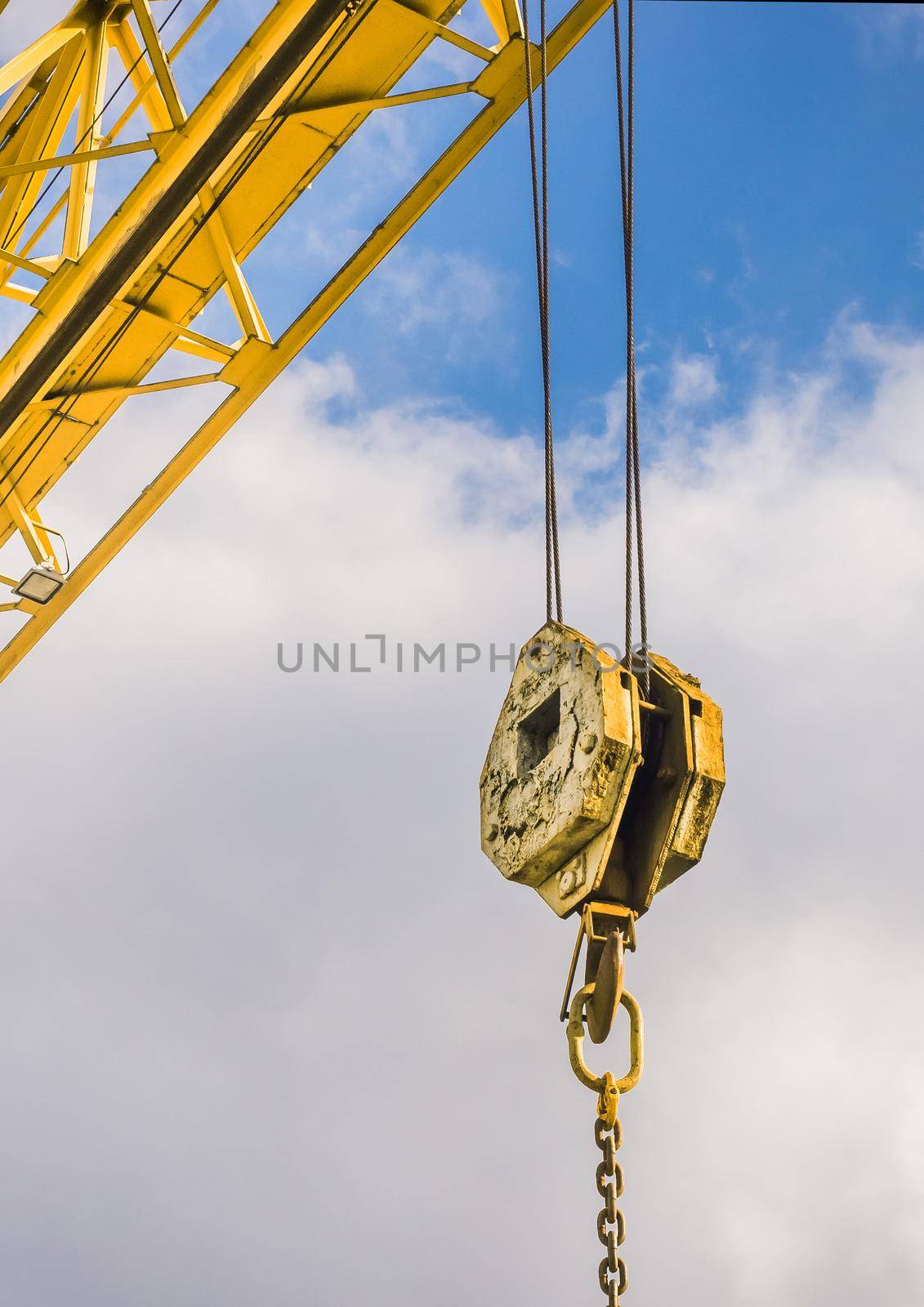 Overhead crane hoist industrial mechanism with hook and chain on a background of blue sky with clouds, close-up.