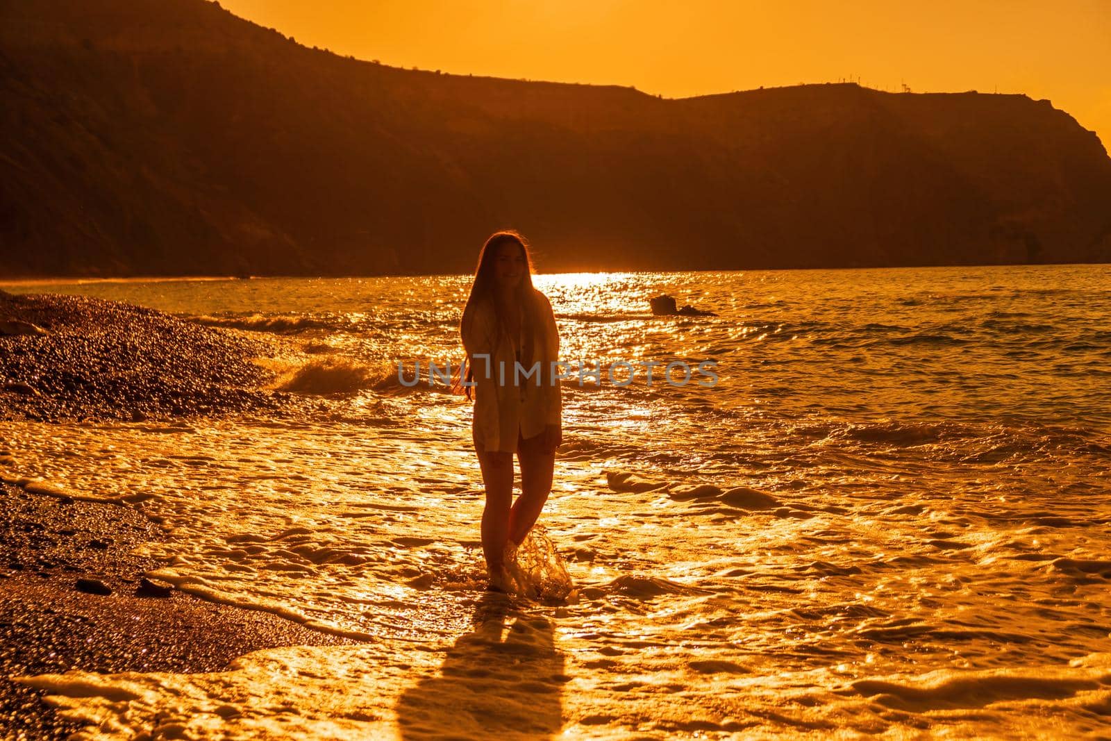 Selective focus. Happy carefree sensual woman with long hair in black swimwear posing at sunset beach. Silhouette of young beautiful playful positive woman outdoor. Summer vacation and trip concept.