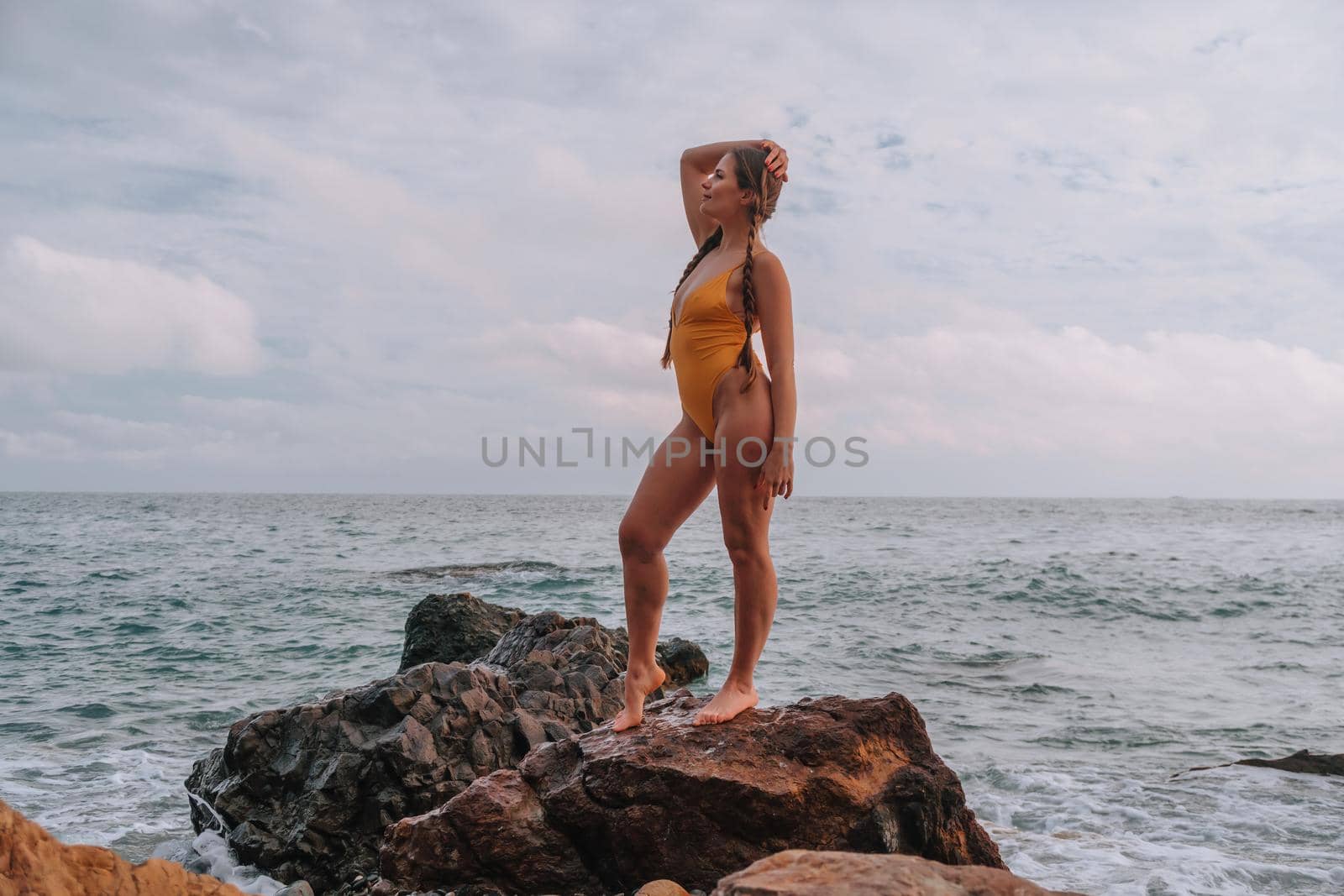 Selective focus. Happy carefree sensual woman with long hair in black swimwear posing at sunset beach. Silhouette of young beautiful playful positive woman outdoor. Summer vacation and trip concept.