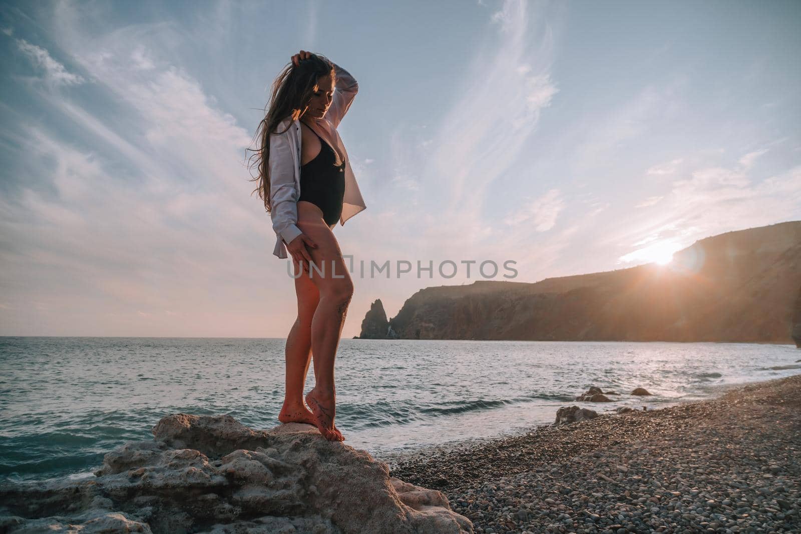 Selective focus. Happy carefree sensual woman with long hair in black swimwear posing at sunset beach. Silhouette of young beautiful playful positive woman outdoor. Summer vacation and trip concept.