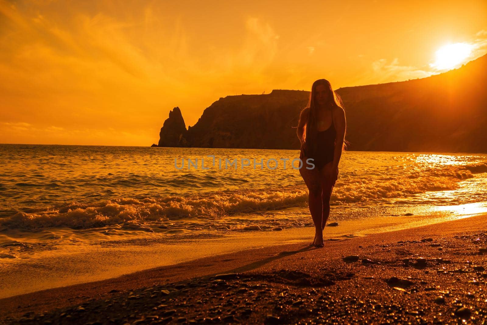 Selective focus. Happy carefree sensual woman with long hair in black swimwear posing at sunset beach. Silhouette of young beautiful playful positive woman outdoor. Summer vacation and trip concept.