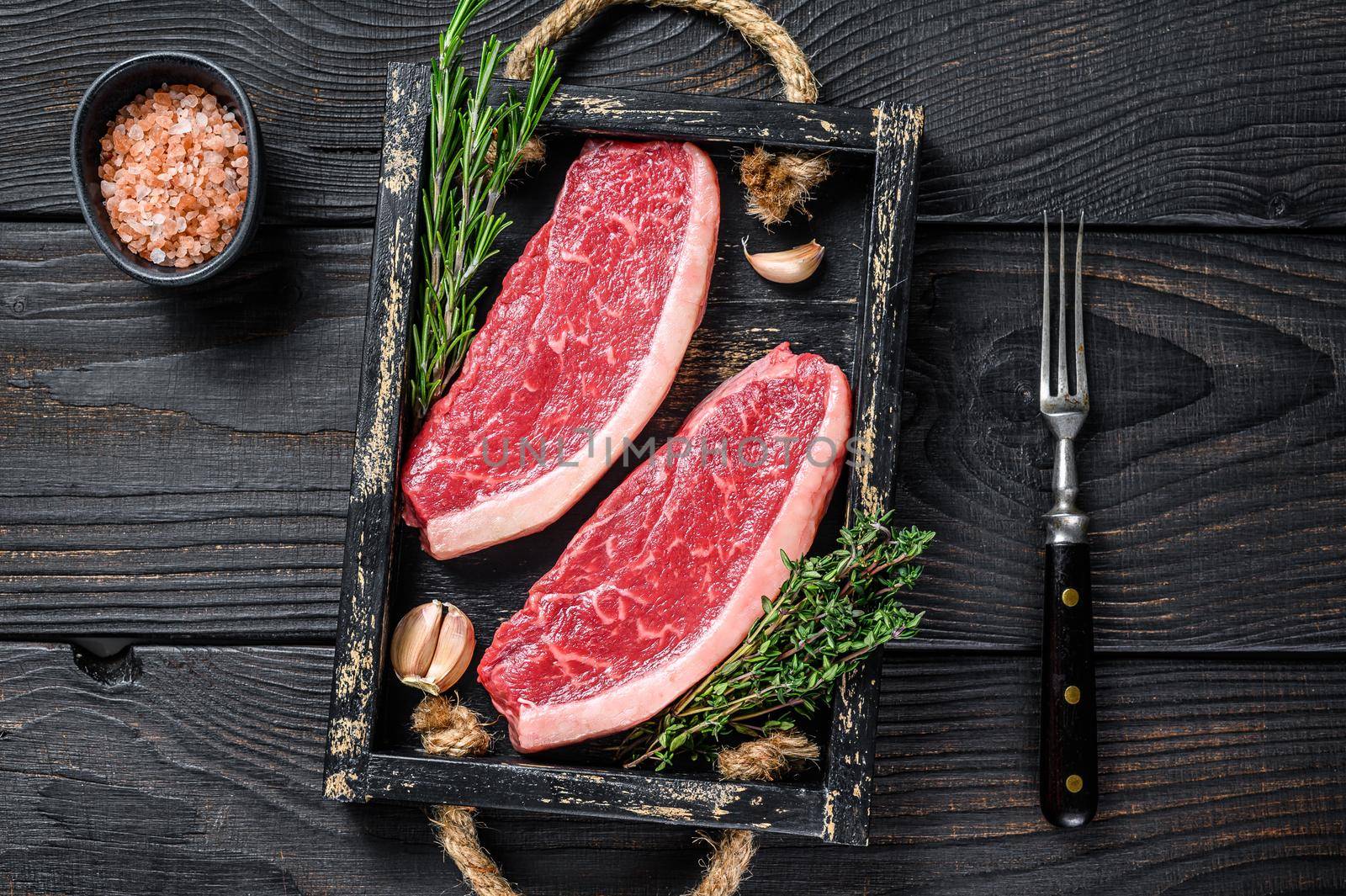 Raw brazilian picanha steak or top sirloin beef meat steak in a wooden tray. Black wooden background. Top view by Composter