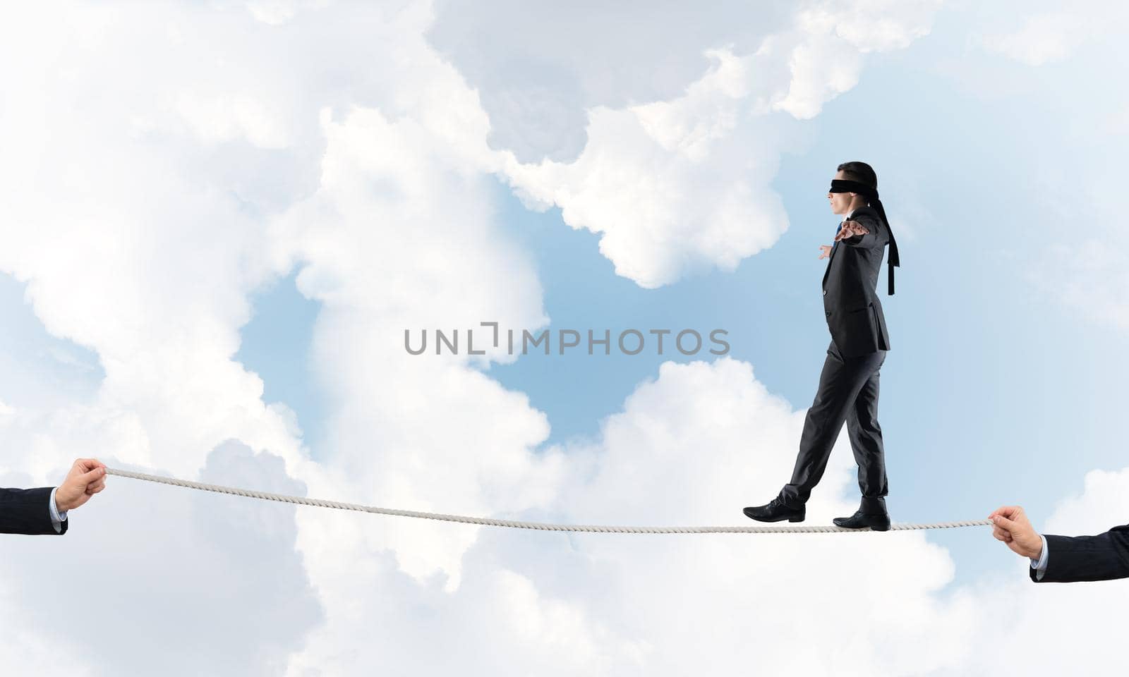 Businessman with blindfolder on eyes walking on rope over sky background
