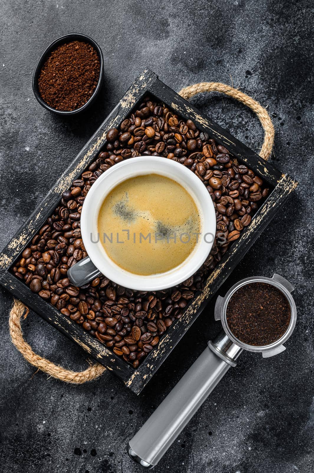 Coffee cup and beans in old wooden tray. Black background. Top view.