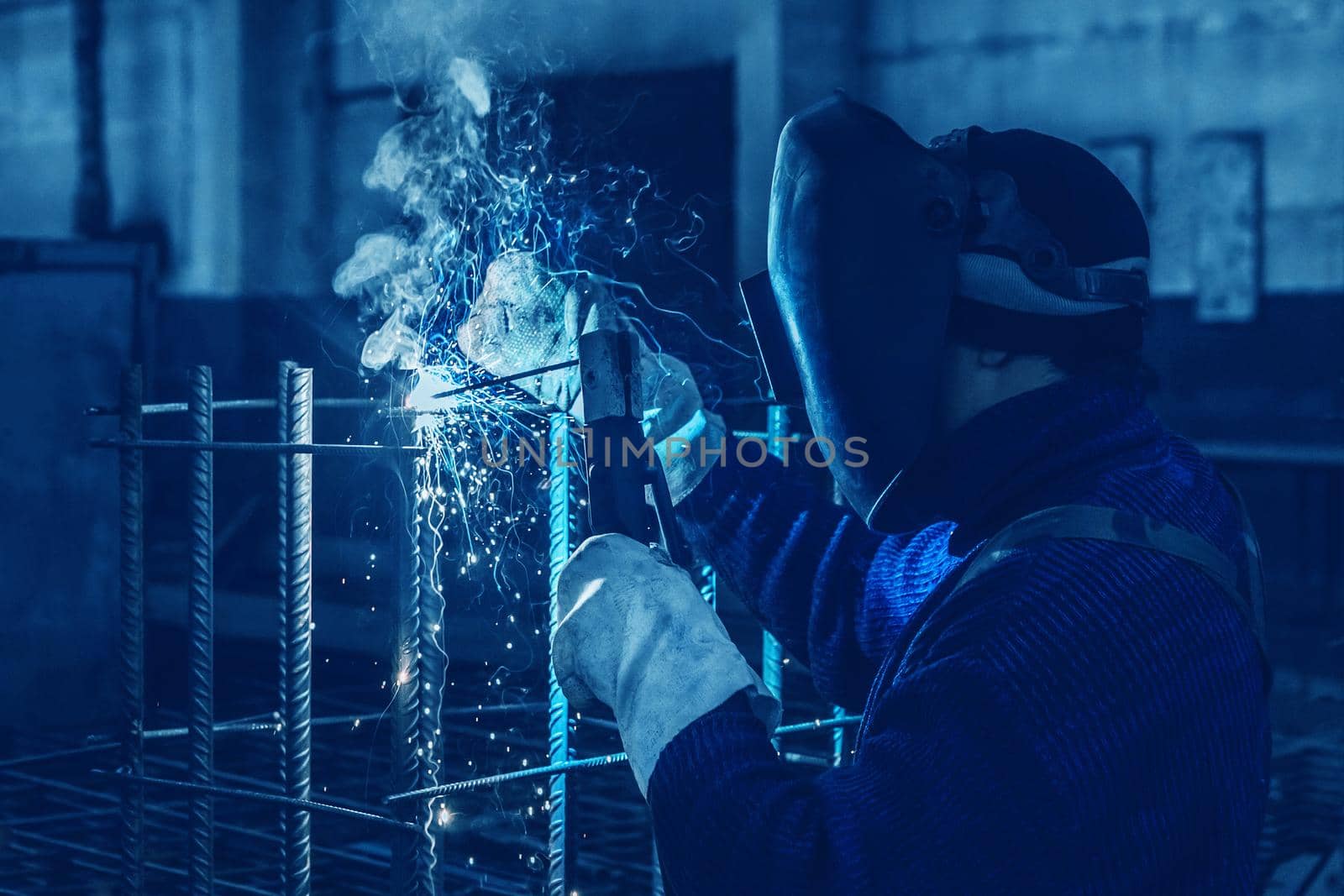 Working man is doing welding work on metal structures in a factory or industrial enterprise.