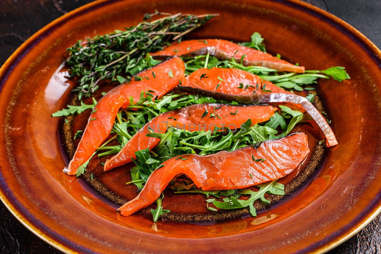 Salad with arugula and smoked salmon fillet slices. Dark background. Top view by Composter