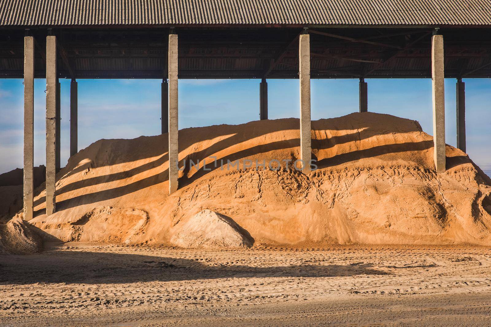 A large pile of sand under a canopy of slate storage on industrial warehouse at a construction site.