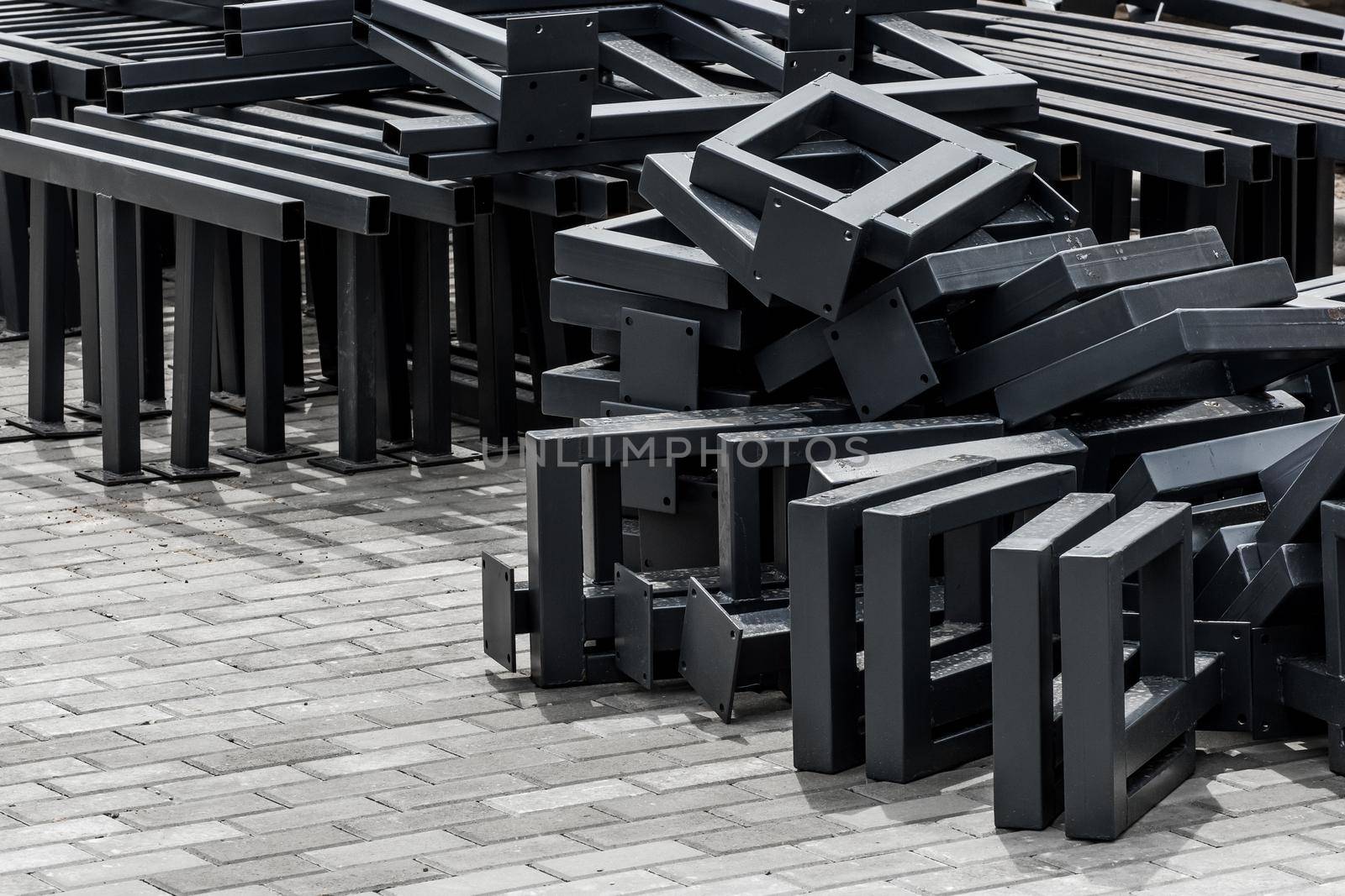 Pile of new metal structures or steel industrial material on paving slabs sidewalk at construction site.