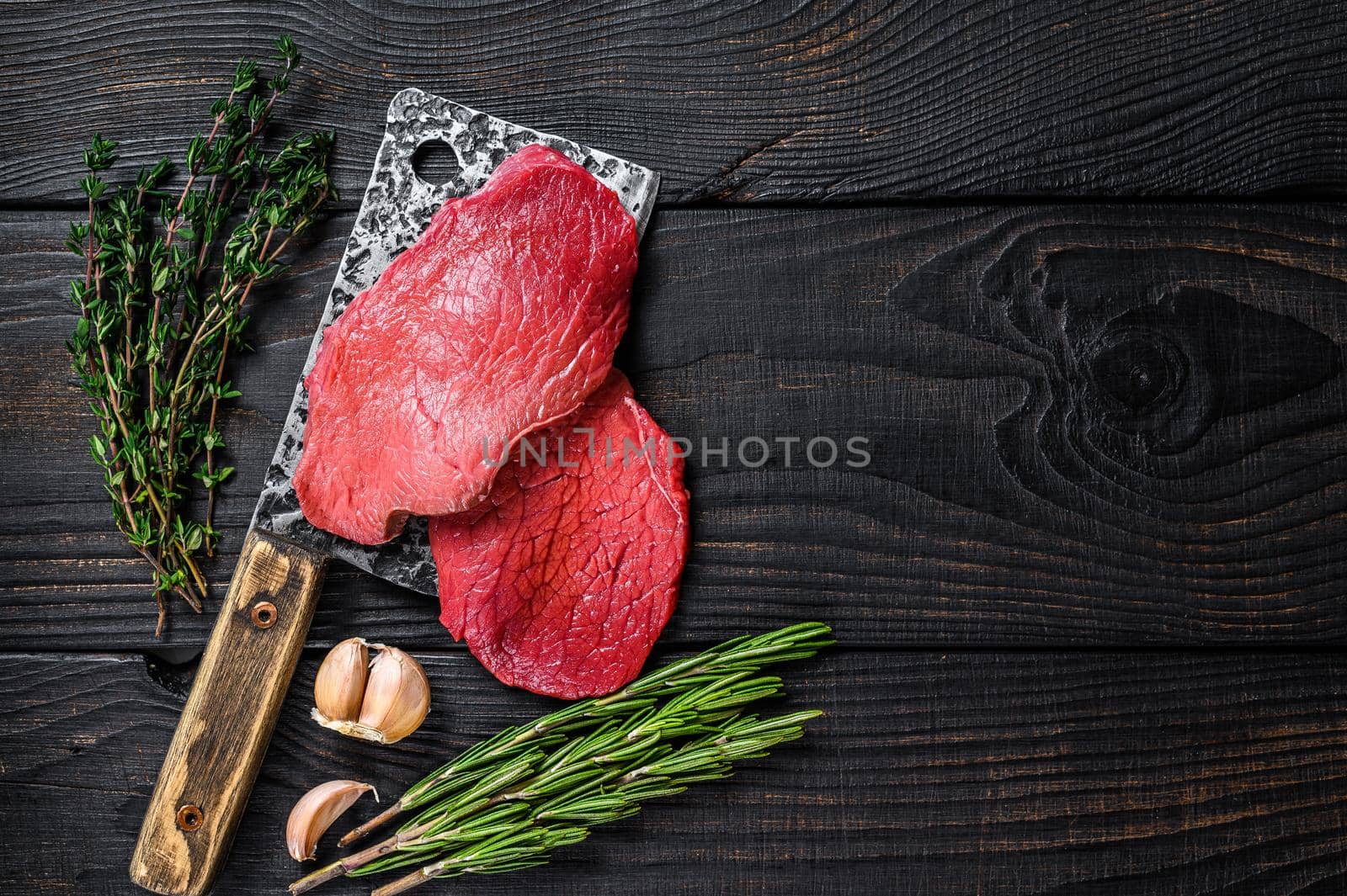 Raw marble beef meat fillet steak on butcher cleaver. Black wooden background. Top view. Copy space by Composter