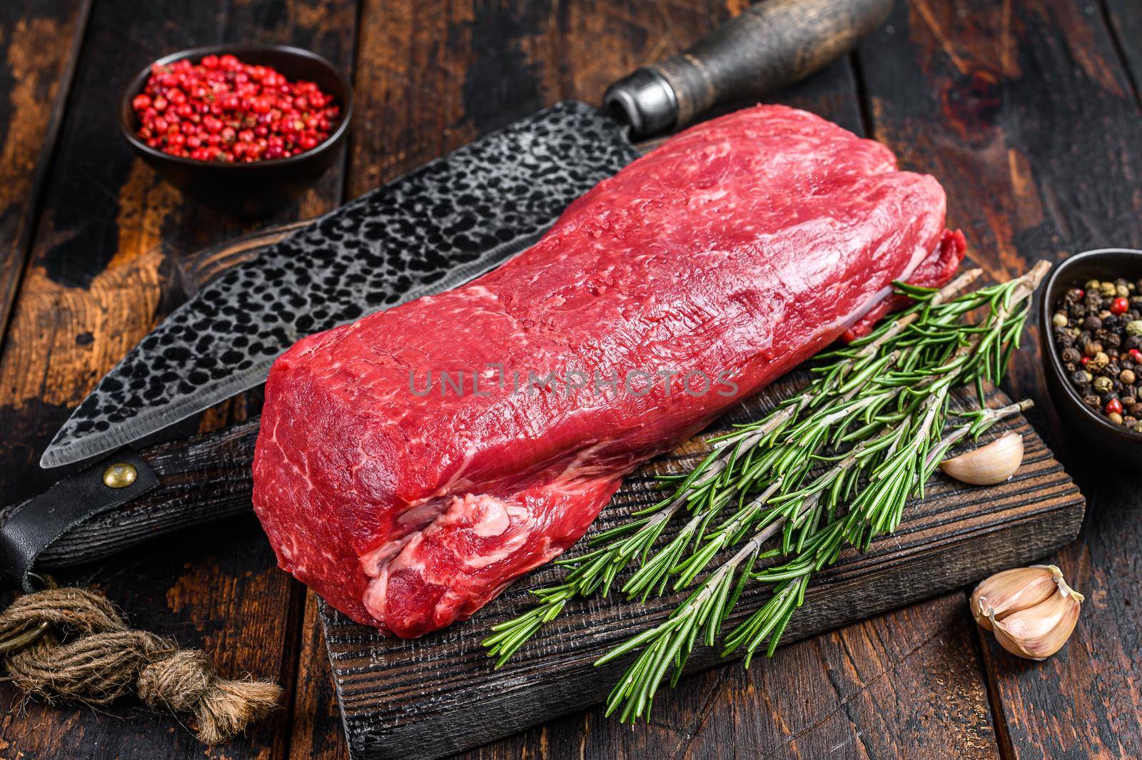 Whole Raw Tenderloin beef meat for steaks fillet mignon on a wooden cutting board with butcher knife. Dark wooden background. Top view.