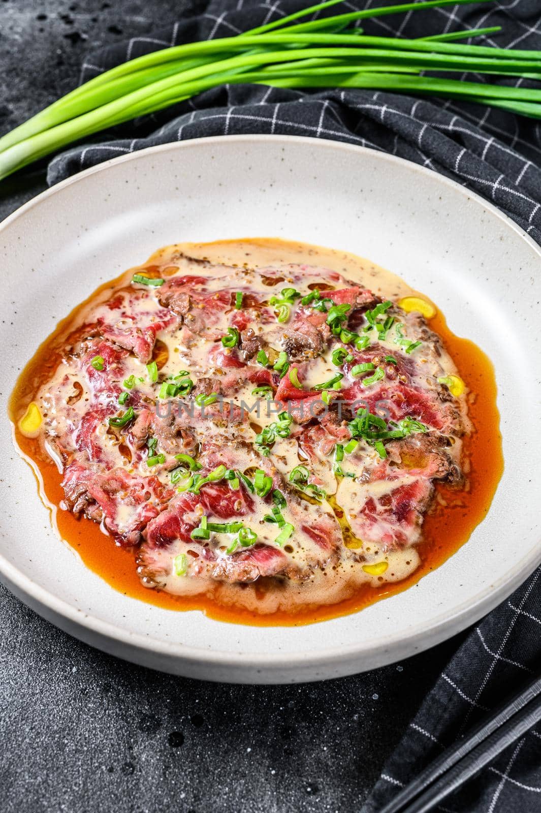 beef carpaccio with fresh green onions. Black background. Top view.