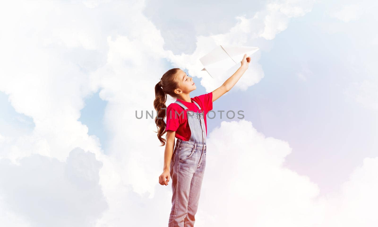 Cute kid girl in overalss with paper plane in hand