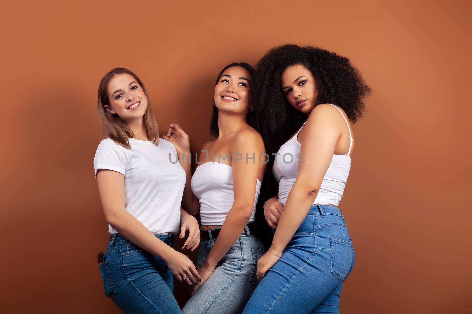 young pretty asian, caucasian, afro woman posing cheerful together on brown background, lifestyle diverse nationality people concept closeup