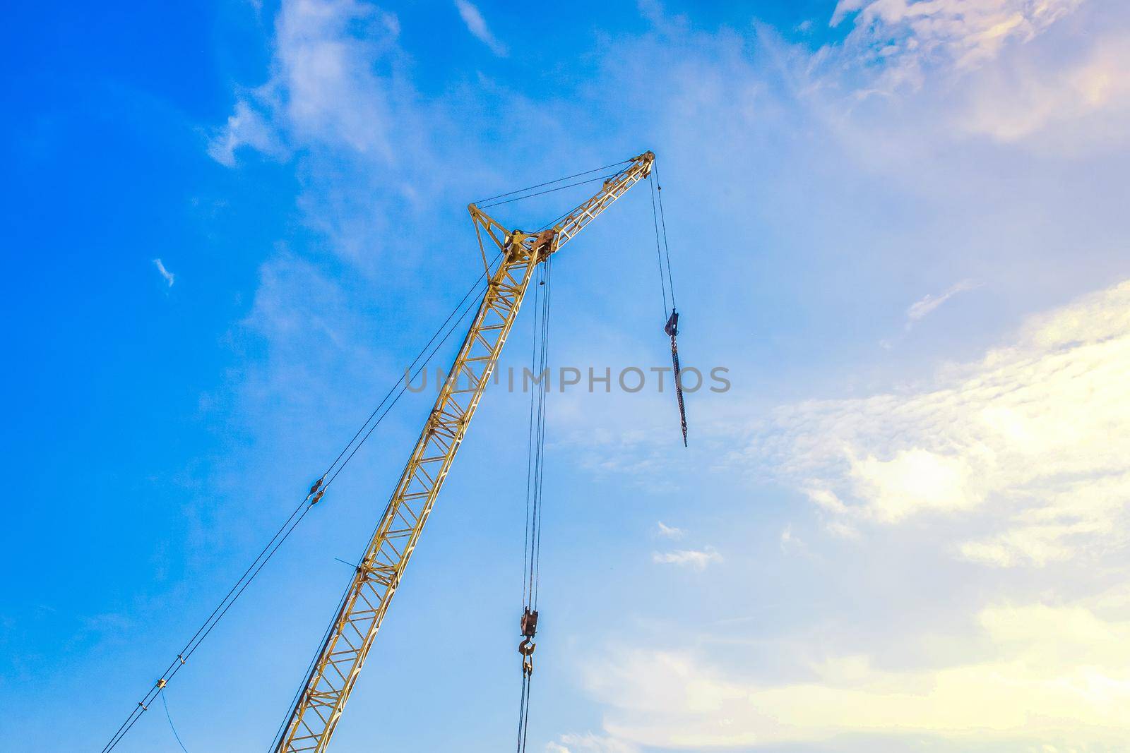 Hoisting machine industrial crane equipment against blue sky at construction site by AYDO8