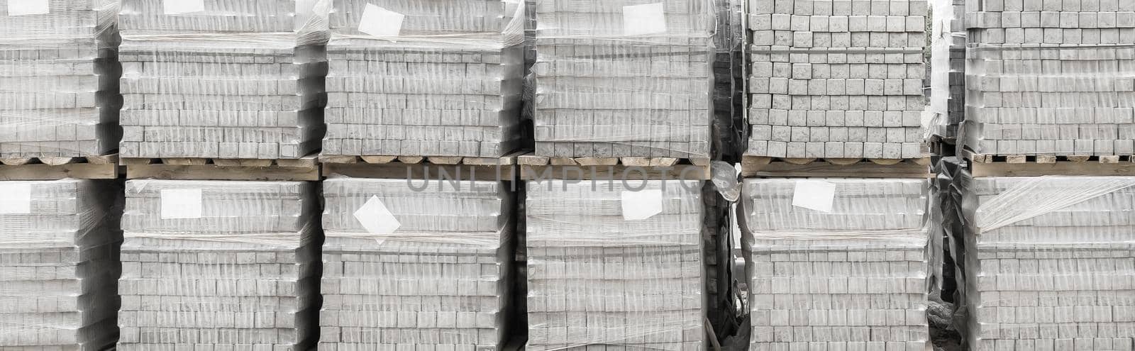 Pile of packaged paving stone slabs industrial material on pallets at construction site.