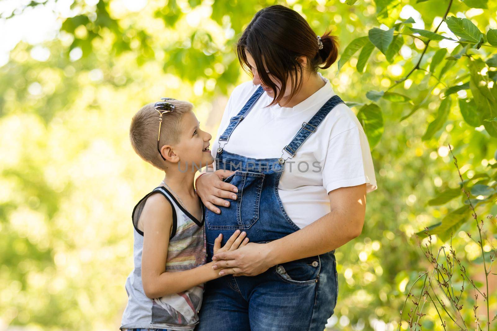 Young and pregnant mother with her son in summer park