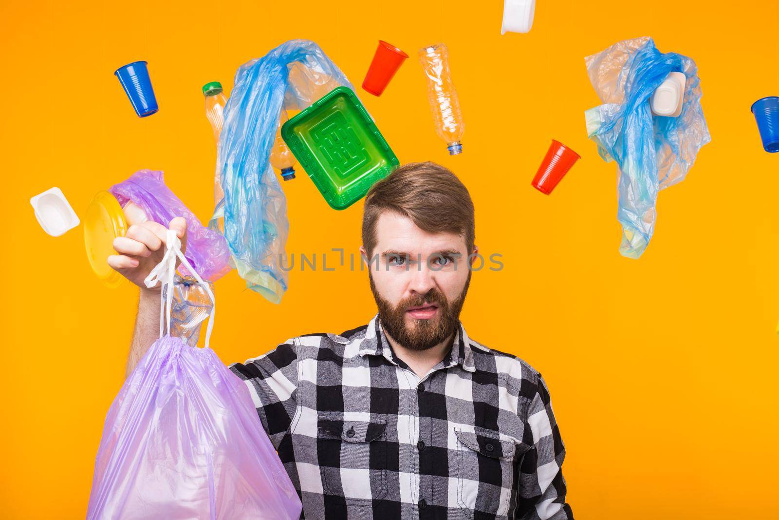 World Environment Day, plastic recycling problem and environmental disaster concept - Angry man holding garbage bag for recycling and showing thumb down on yellow background.
