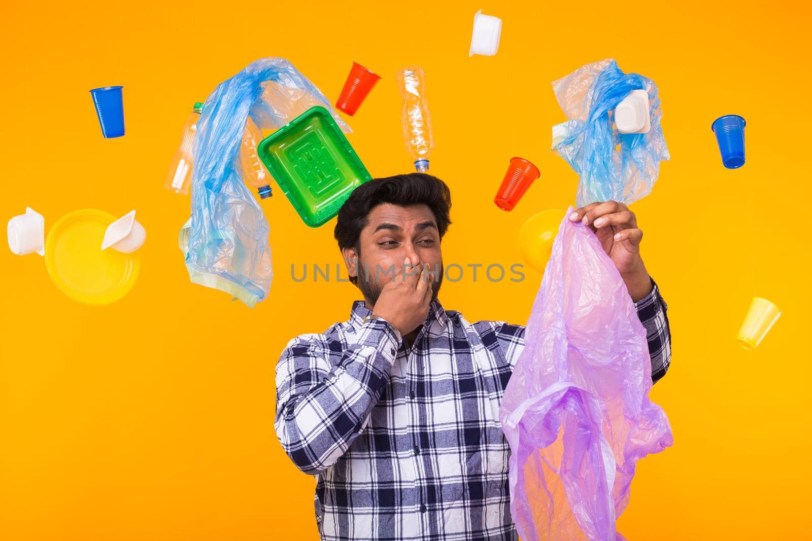 World Environment Day, plastic recycling problem and environmental disaster concept - Upset Indian man closing nose because he is felt bad smell from garbage on yellow background