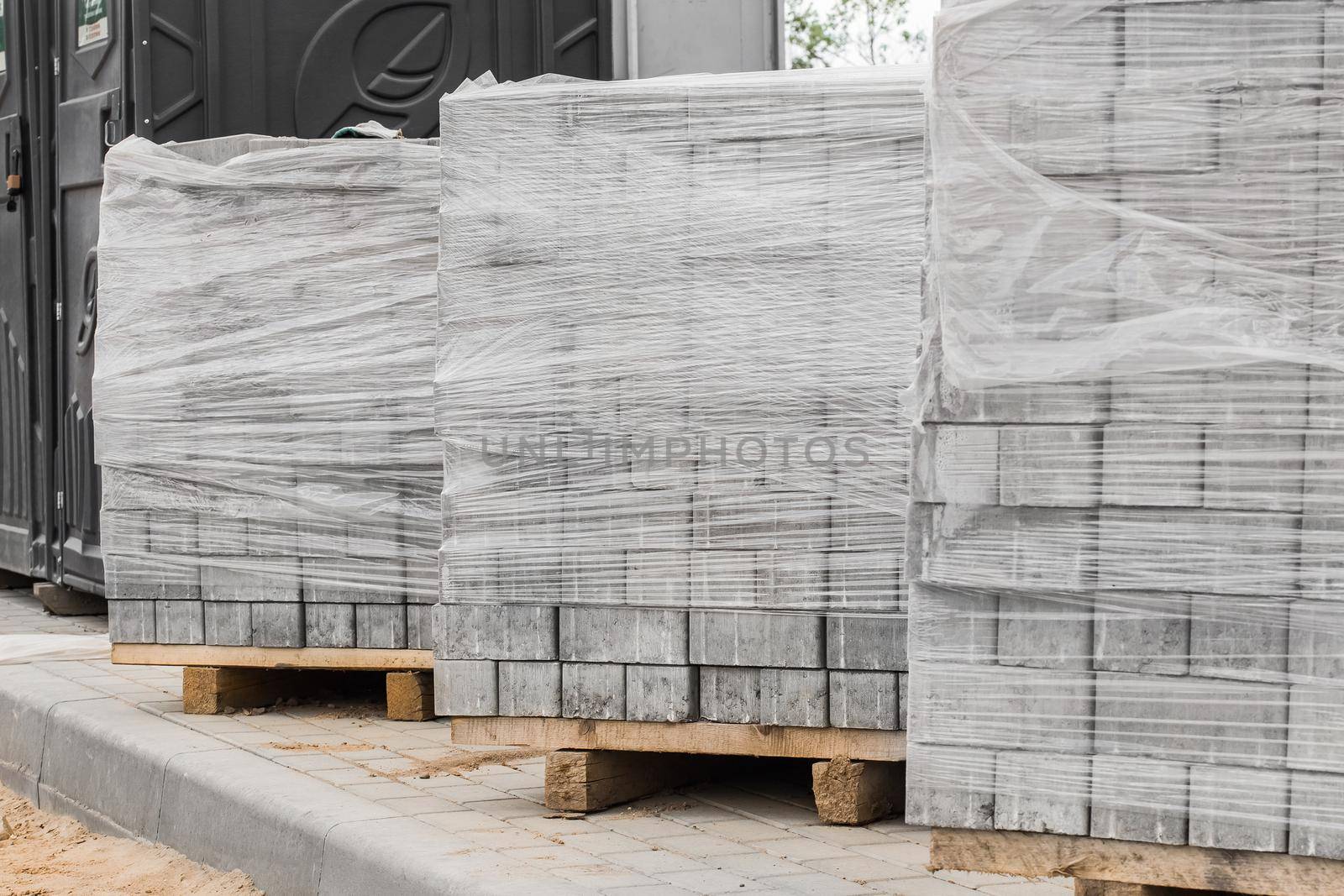 A pile of new paving slabs on a wooden pallet wrapped in plastic wrap. Building materials at the construction site by AYDO8