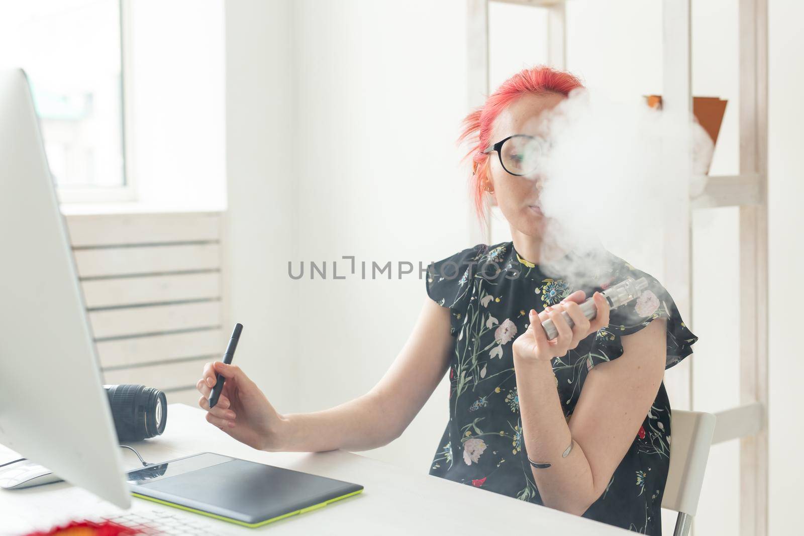 graphic designer concept - Female graphic designer working on computer while using graphic tablet at desk in the office and smoking a vape.