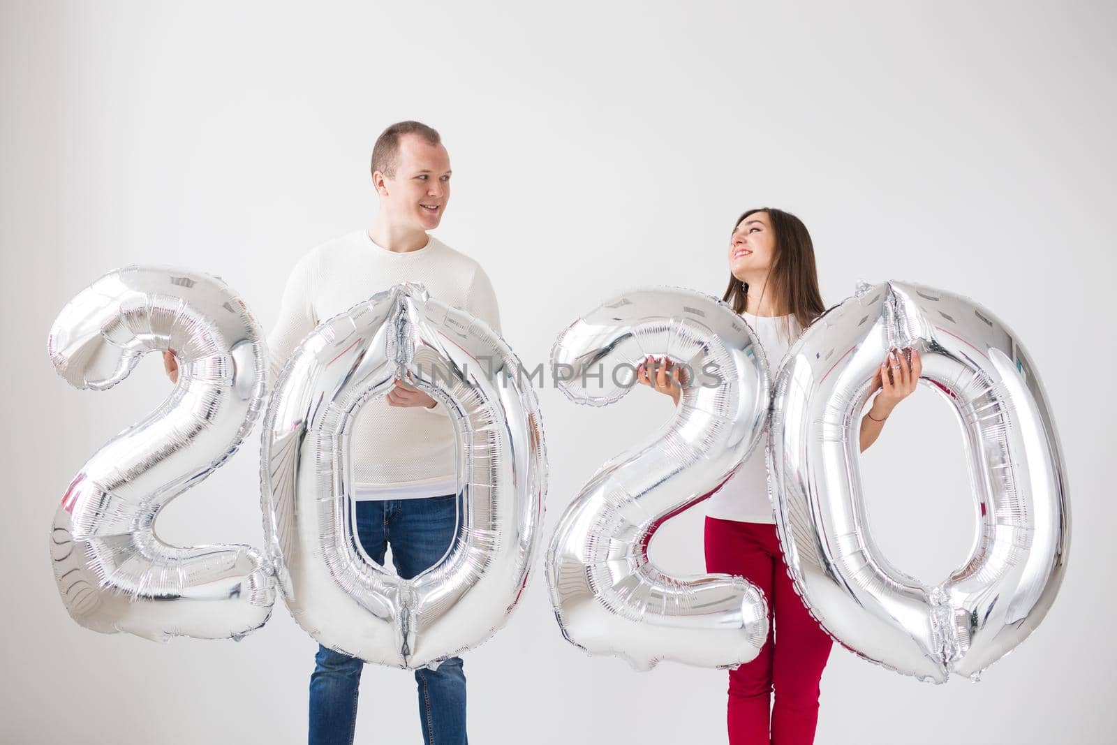 New year, celebration and holidays concept - love couple having fun with sign 2020 made of silver balloons for new year on white background by Satura86
