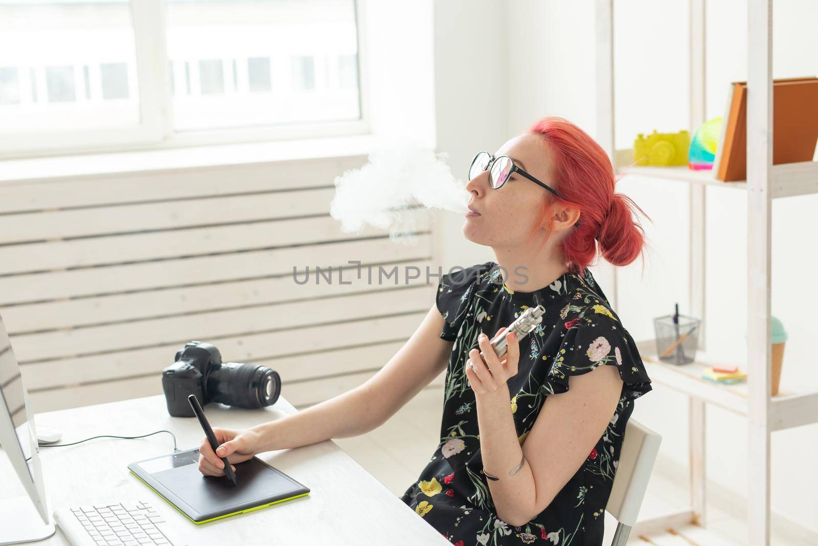graphic designer concept - Female graphic designer working on computer while using graphic tablet at desk in the office and smoking a vape.